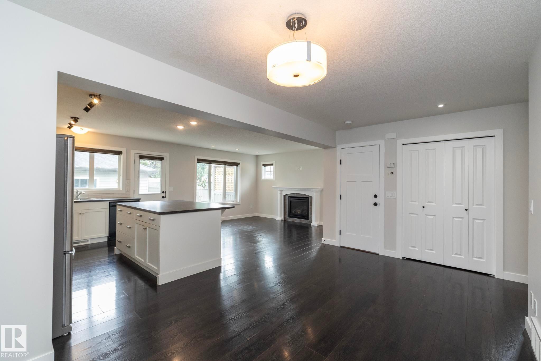 Dark wood-finish flooring, white kitchen cabinetry, a kitchen island with dark countertop, a built-in fireplace, and a ceiling-mounted light fixture - 55 Michigan Street, Devon, AB
