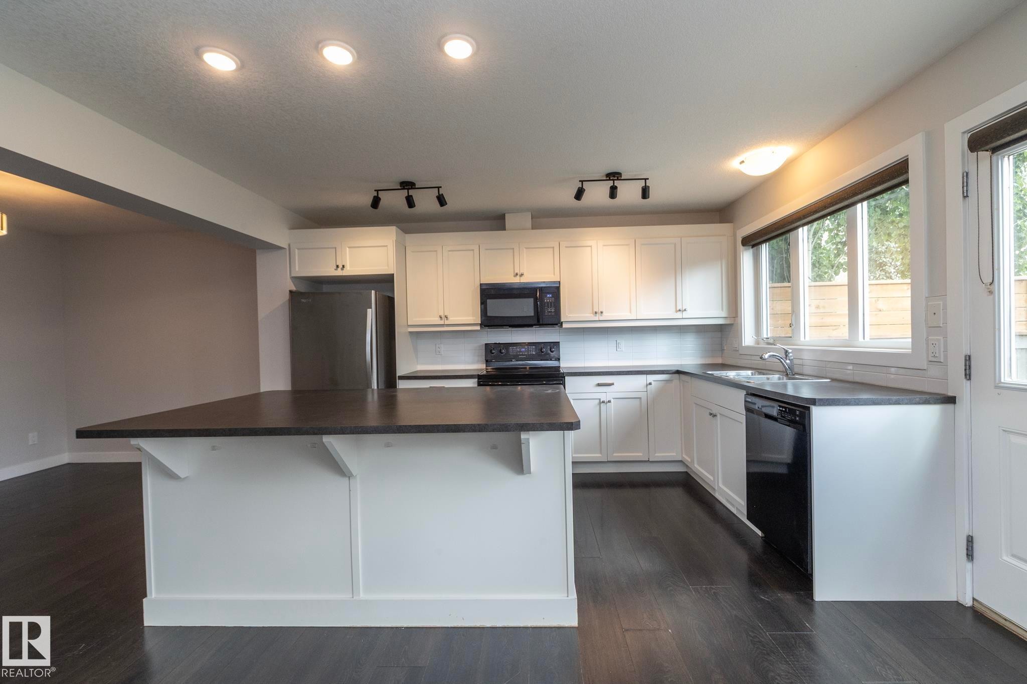 Kitchen featuring a central island, white cabinetry, dark countertops, and stainless steel appliances - 55 Michigan Street, Devon, AB