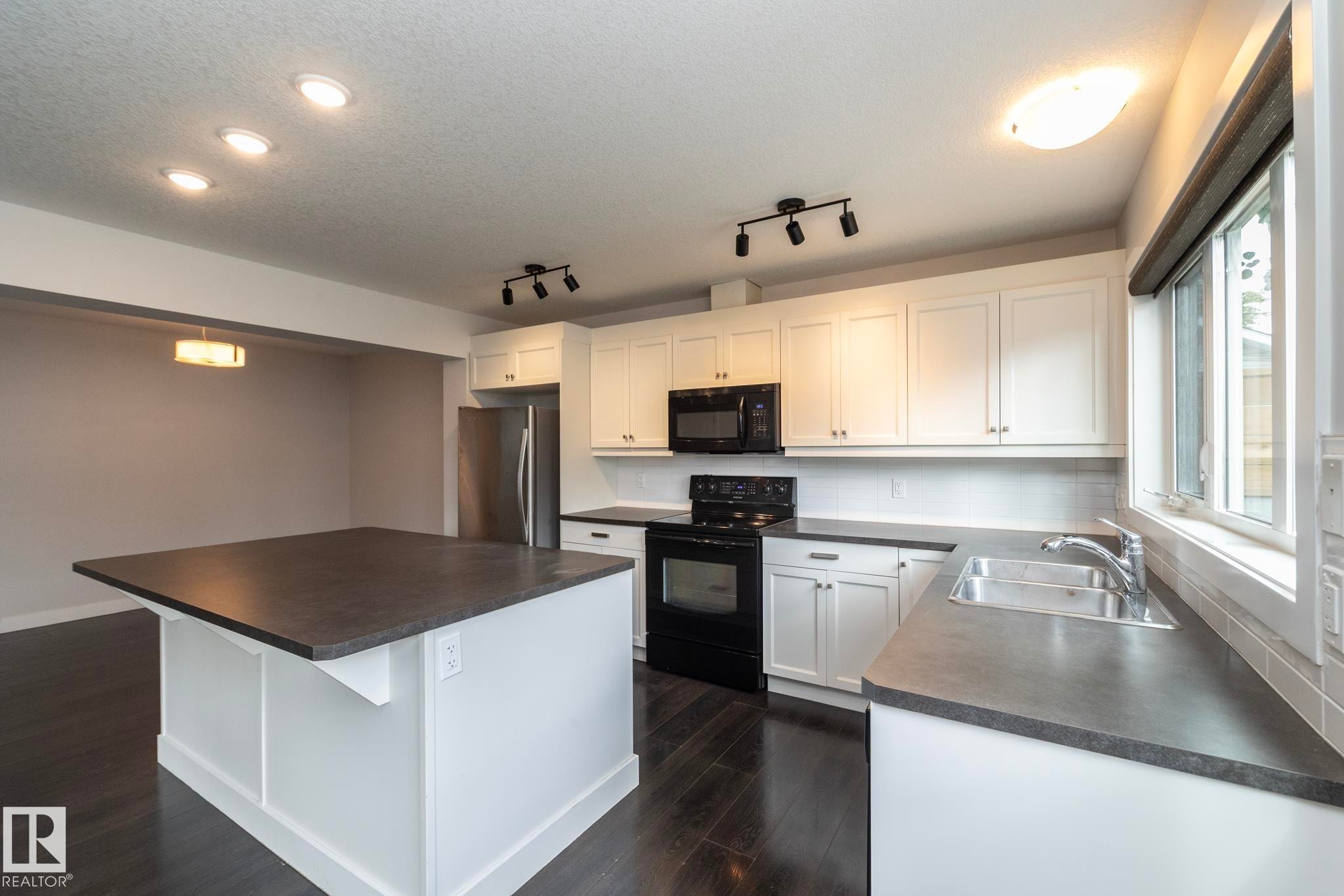 Bright kitchen featuring white cabinetry, dark countertops, dark wood-finish flooring, a stainless steel refrigerator, and a kitchen island - 55 Michigan Street, Devon, AB