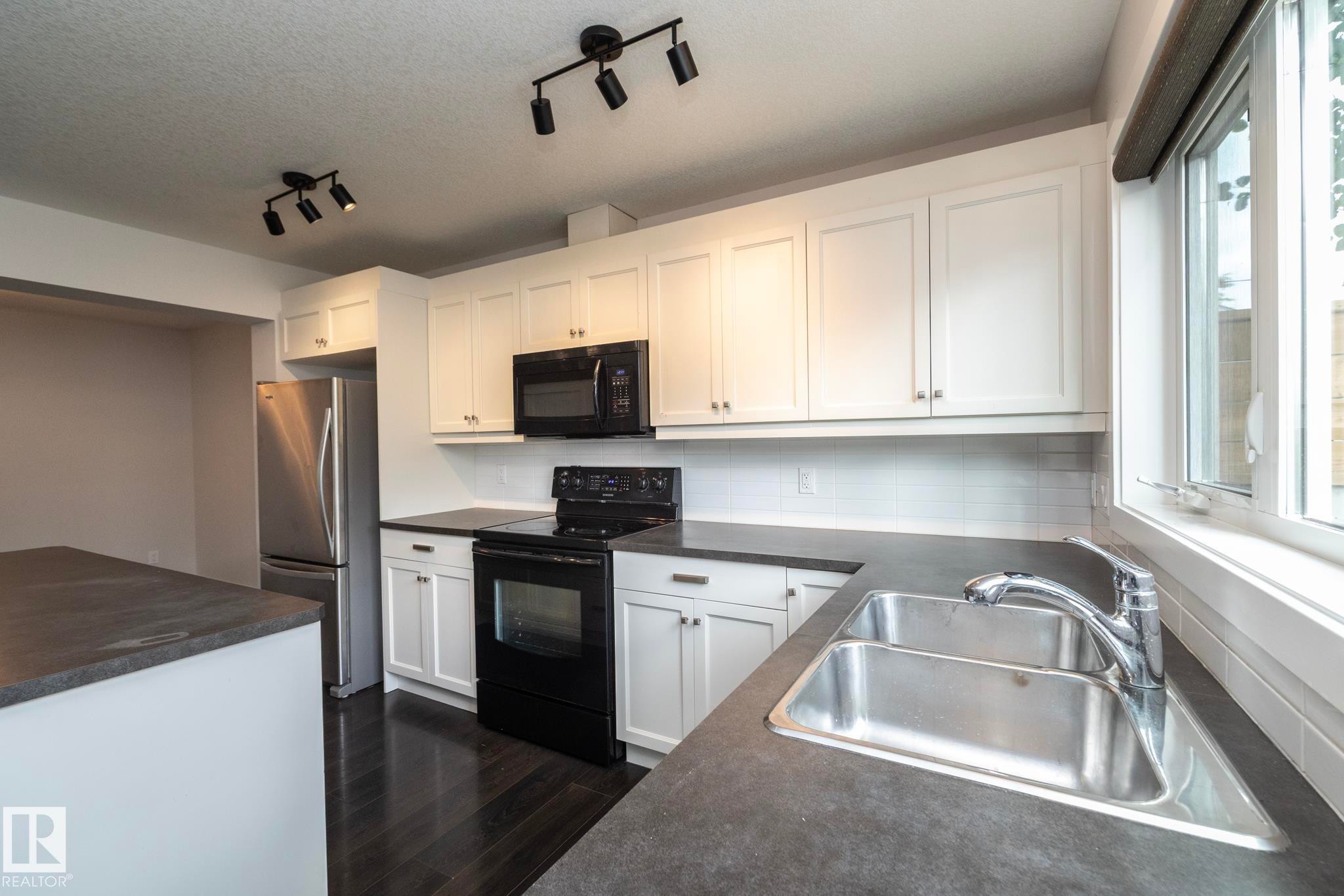 White cabinetry, dark countertops, a stainless steel sink, and wood-finish flooring - 55 Michigan Street, Devon, AB