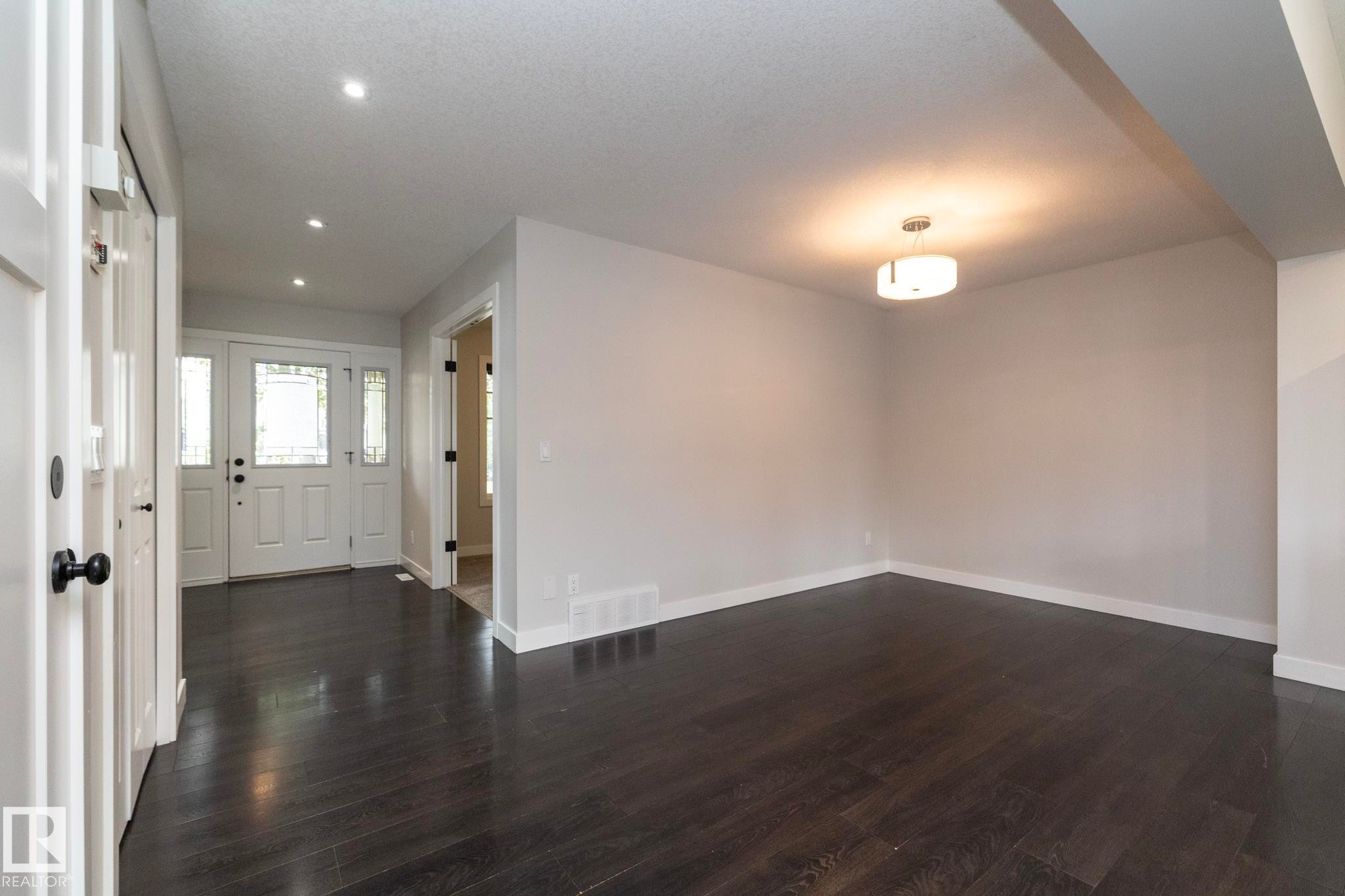 Dark wood-finish flooring throughout, white interior doors with dark hardware, recessed ceiling lighting, and a modern ceiling light fixture - 55 Michigan Street, Devon, AB