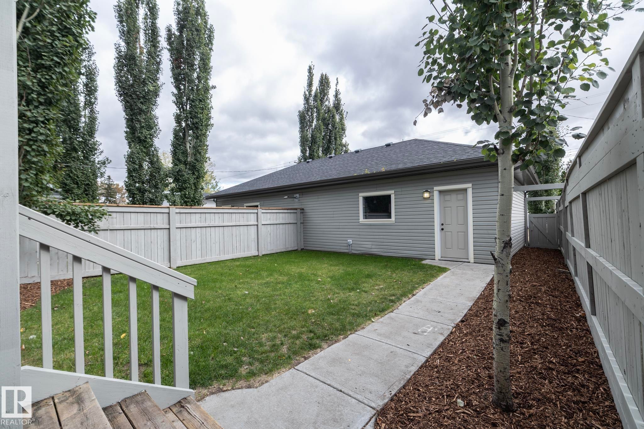 Landscaped backyard with a manicured lawn, concrete pathway, and a privacy fence - 55 Michigan Street, Devon, AB