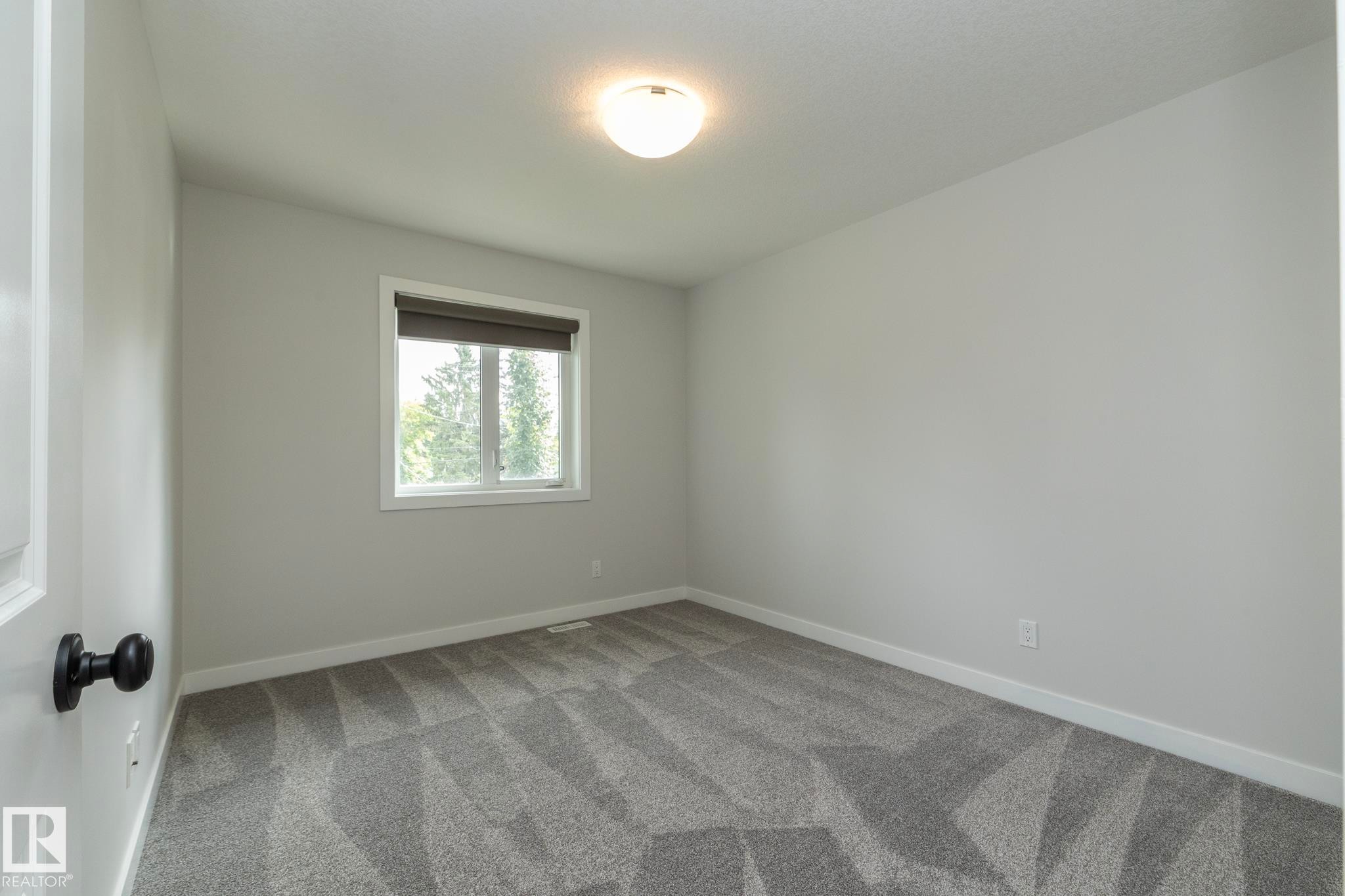 Window with a roller shade, light-colored walls, patterned carpet flooring, and an overhead flush mount light fixture - 55 Michigan Street, Devon, AB