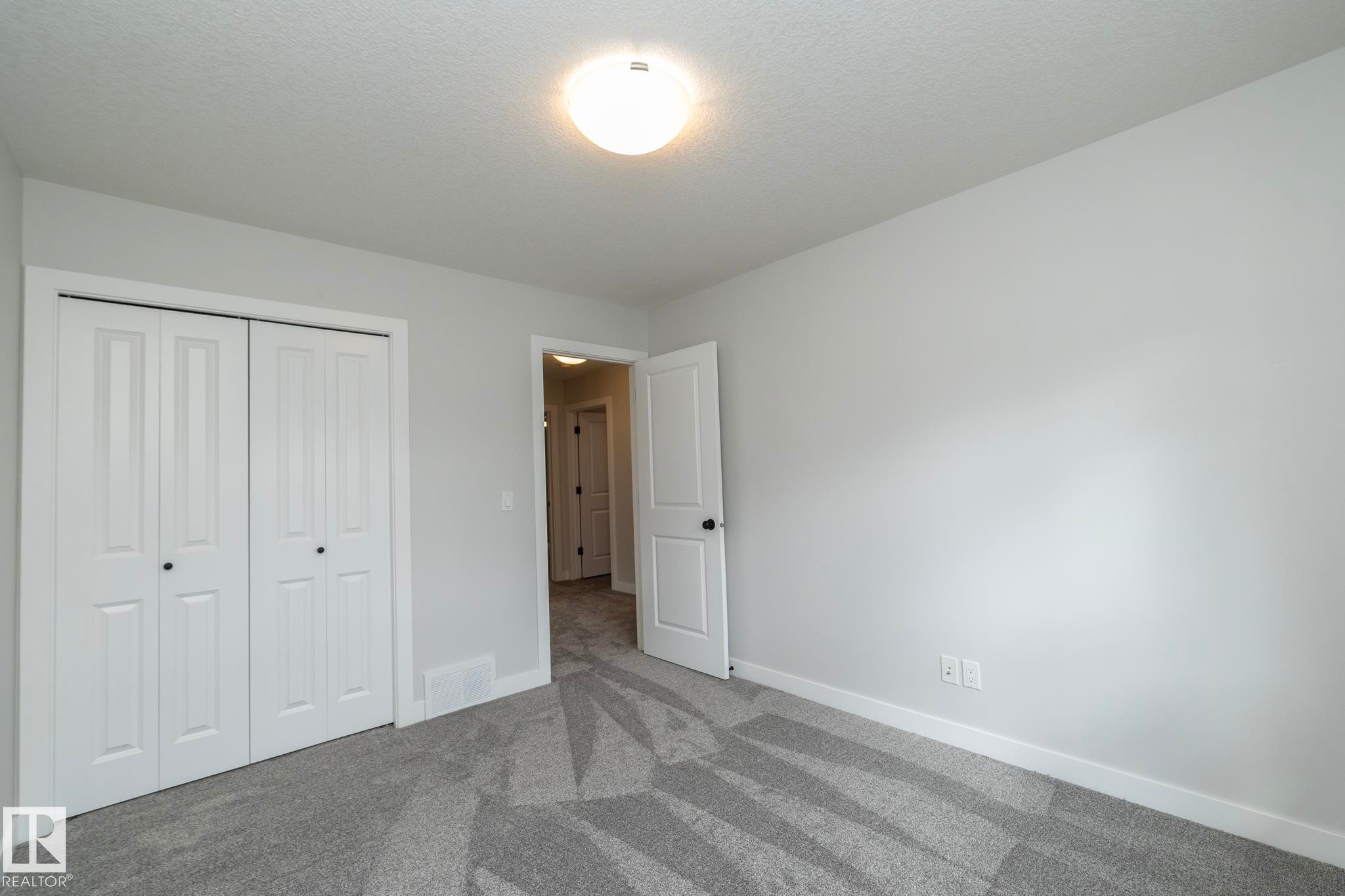 Light gray wall paint, patterned gray carpeting, white bi-fold closet doors, white interior door with black hardware, and a ceiling-mounted light fixture - 55 Michigan Street, Devon, AB