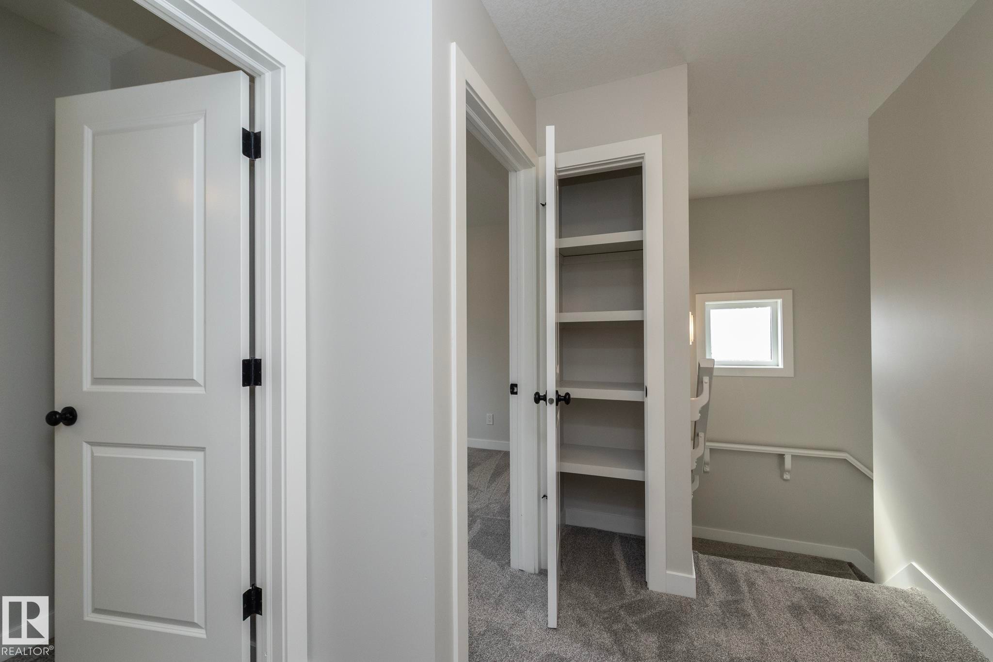 Hallway with carpet flooring, white paneled doors, built-in shelving, and a window providing natural light - 55 Michigan Street, Devon, AB