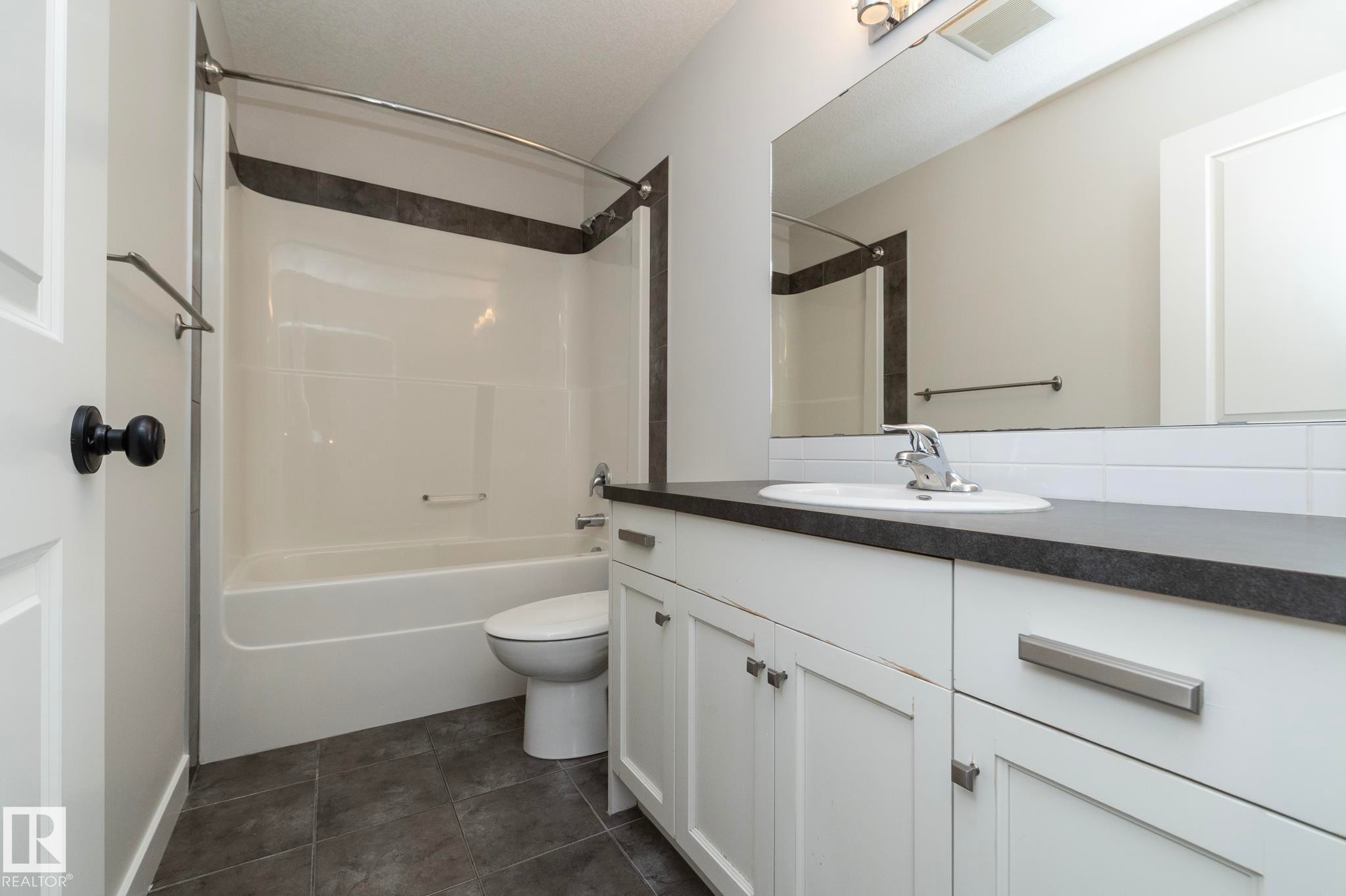 Bathroom featuring a white vanity with a dark countertop, an integrated sink, white subway tile backsplash, and dark tile flooring - 55 Michigan Street, Devon, AB