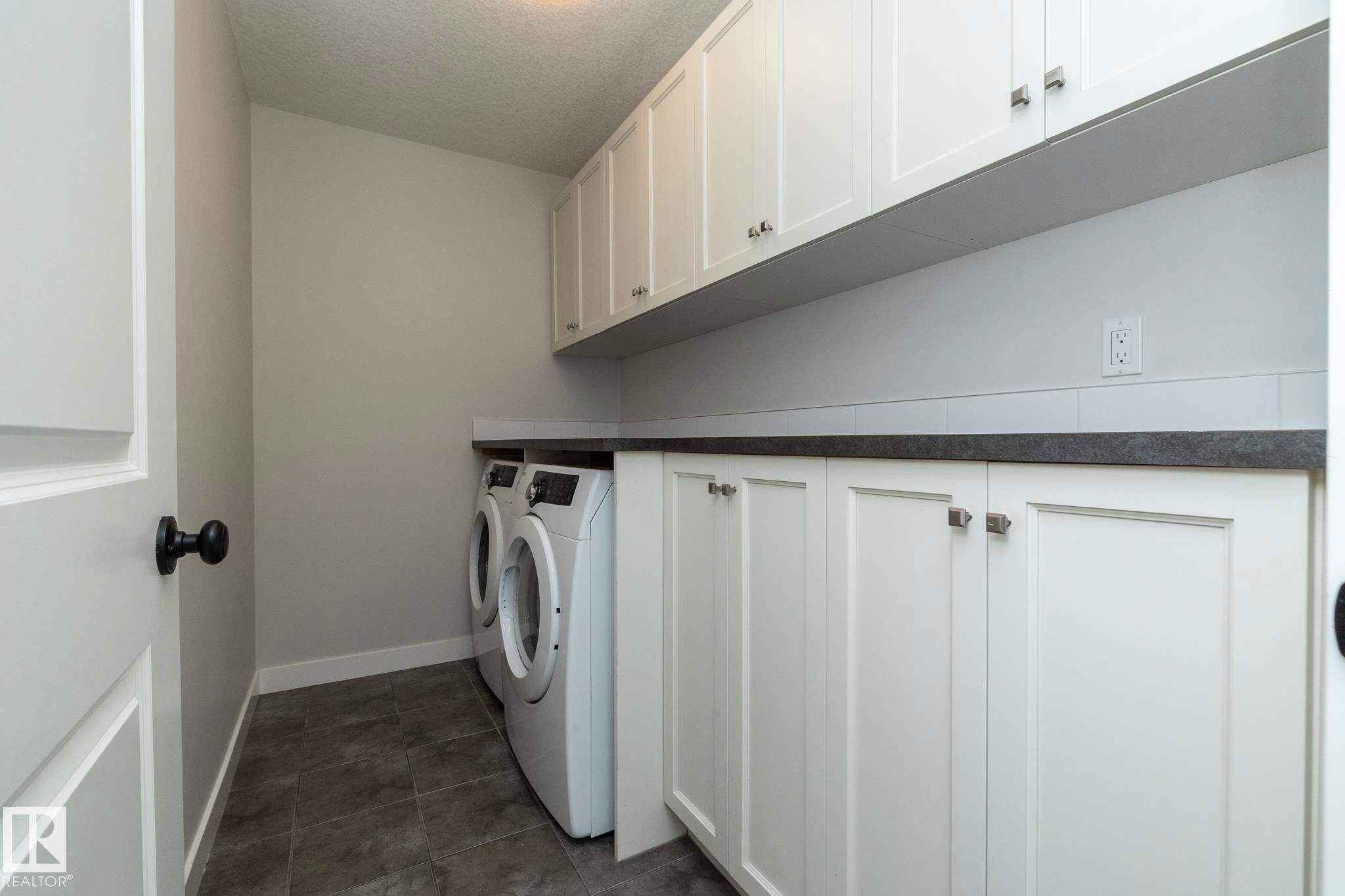 Laundry area featuring white cabinetry, dark countertop, subway tile backsplash, and dark tile flooring - 55 Michigan Street, Devon, AB