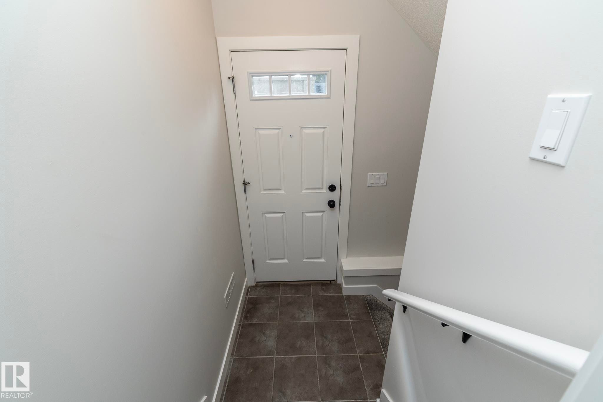Entryway featuring a paneled door with decorative glass, tiled flooring, and a white handrail - 55 Michigan Street, Devon, AB
