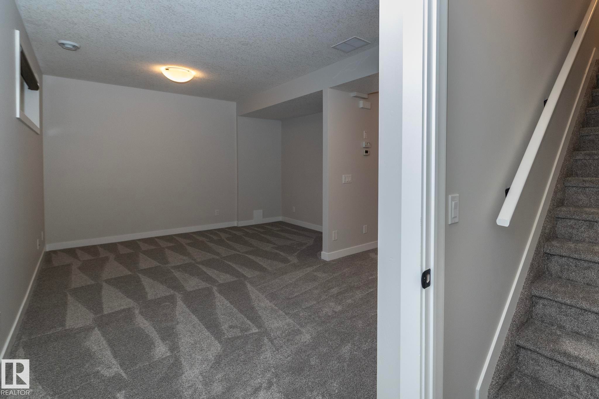 Spacious room with patterned carpeting, neutral wall finishes, and a single light fixture - 55 Michigan Street, Devon, AB