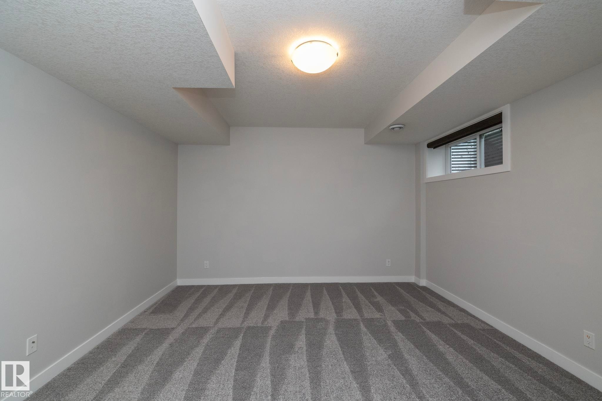 Room featuring patterned gray carpeting, white walls, a single ceiling-mounted light fixture, and a window with blinds - 55 Michigan Street, Devon, AB