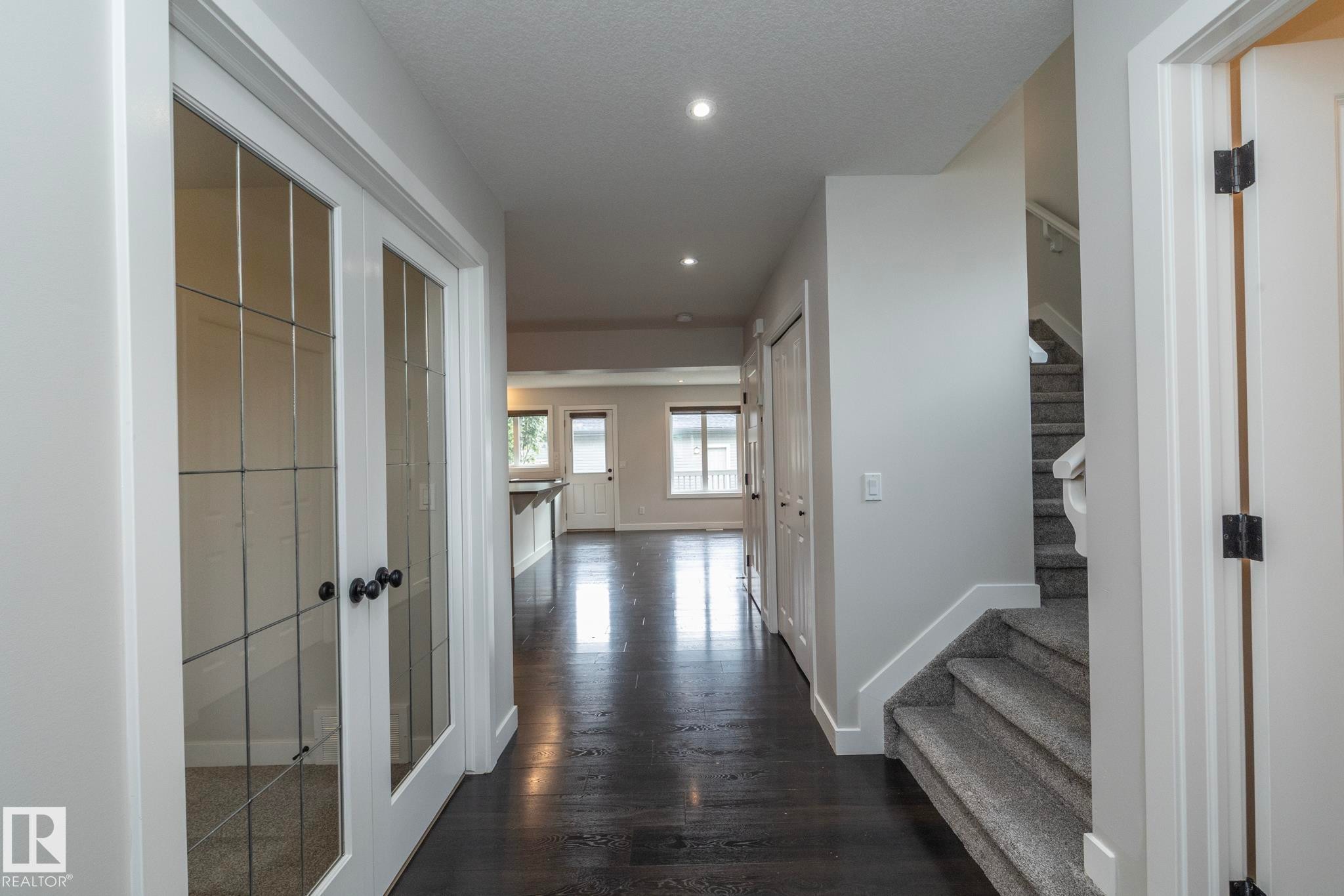 Dark wood-finish flooring, recessed lighting, white trim throughout, and a carpeted staircase - 55 Michigan Street, Devon, AB