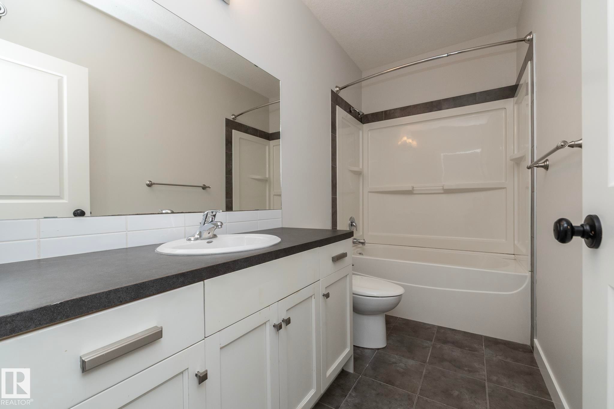 White vanity with a dark countertop and integrated sink, subway tile backsplash, framed mirror, and a white tub with shower surround - 55 Michigan Street, Devon, AB