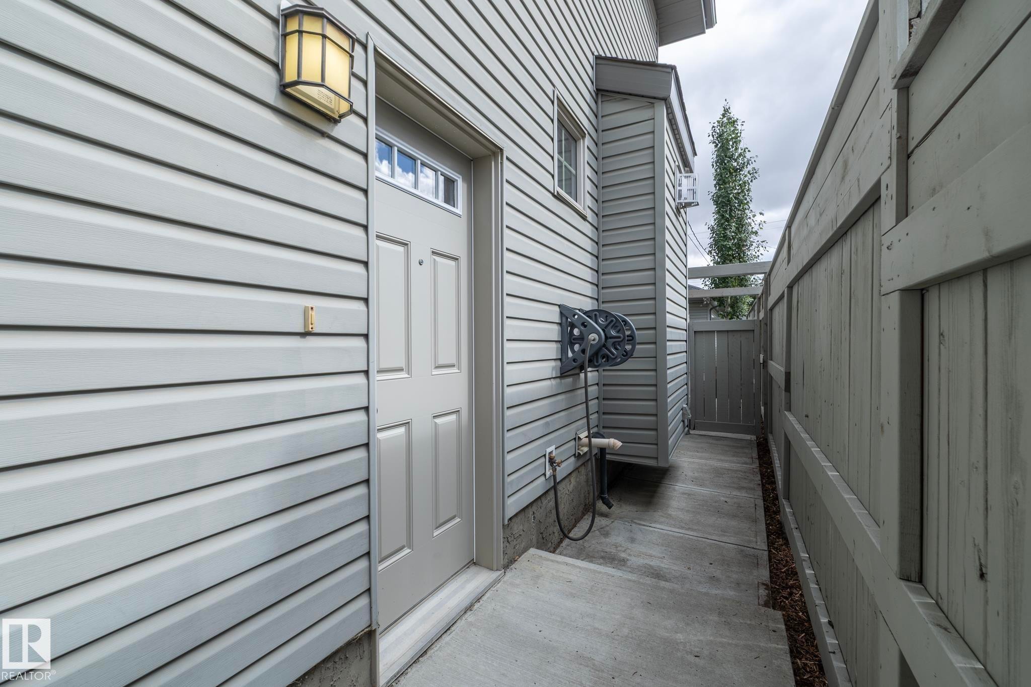 Light-colored horizontal siding exterior with a paneled entry door featuring a transom window, a fixed outdoor wall sconce, and a concrete walkway - 55 Michigan Street, Devon, AB
