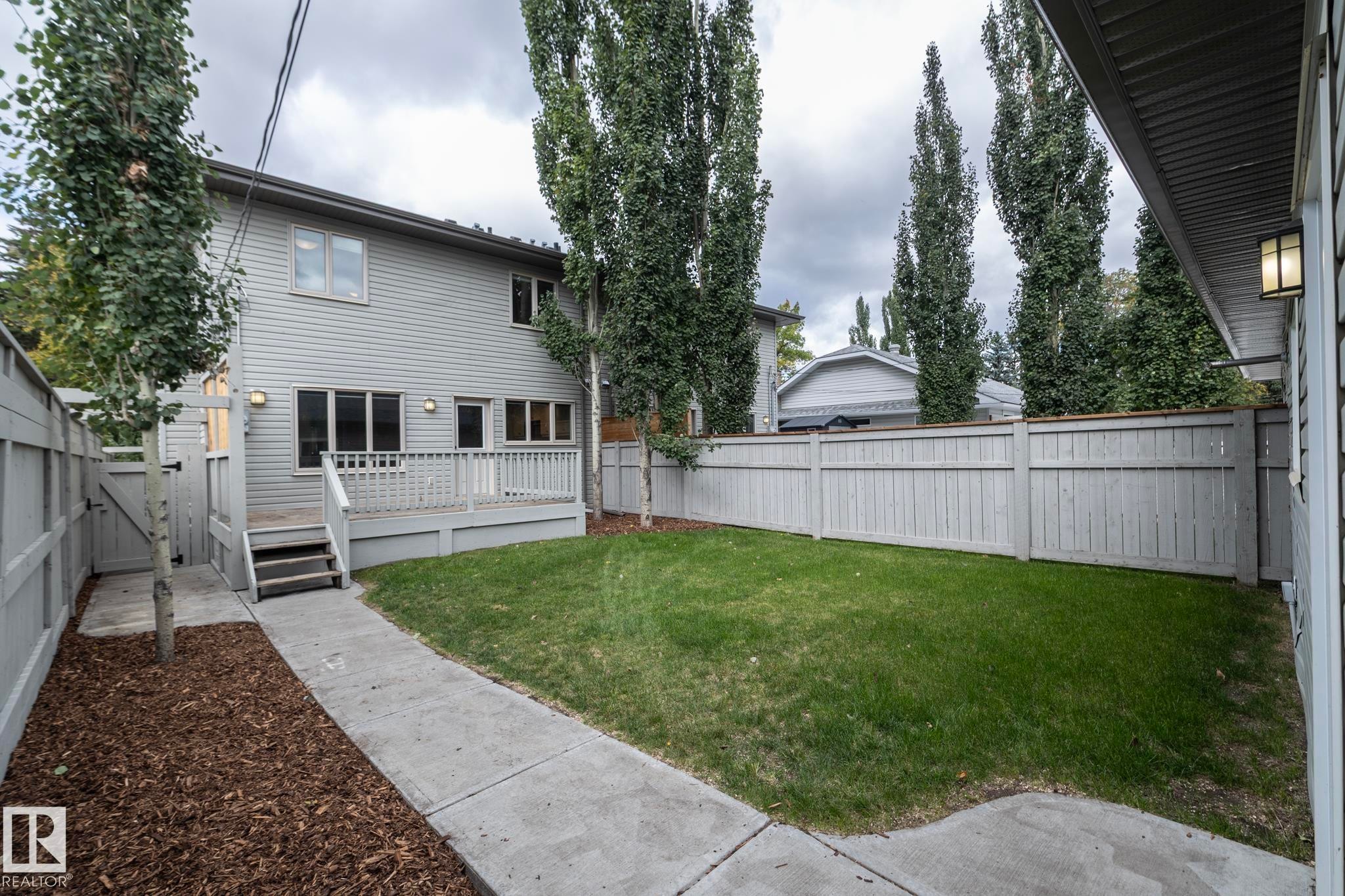 Expansive backyard featuring a manicured lawn, a private wood-plank fence, a raised wood deck with railing, and mature trees - 55 Michigan Street, Devon, AB