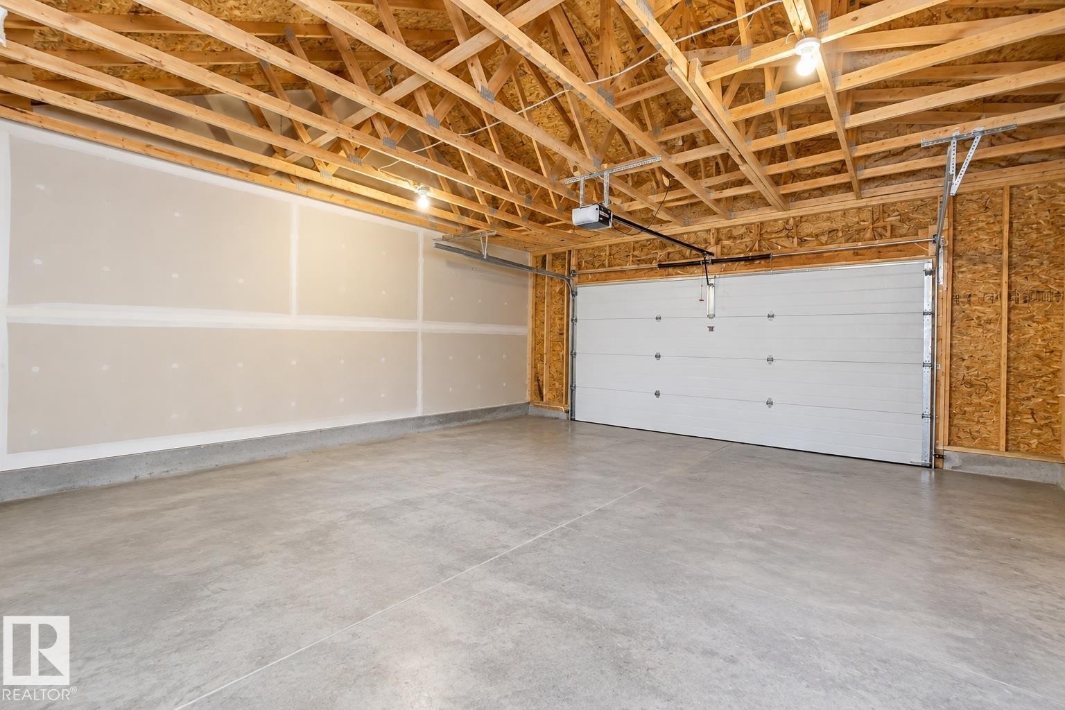 Exposed wood framing, concrete flooring, and a panel garage door with an automatic opener - 55 Michigan Street, Devon, AB