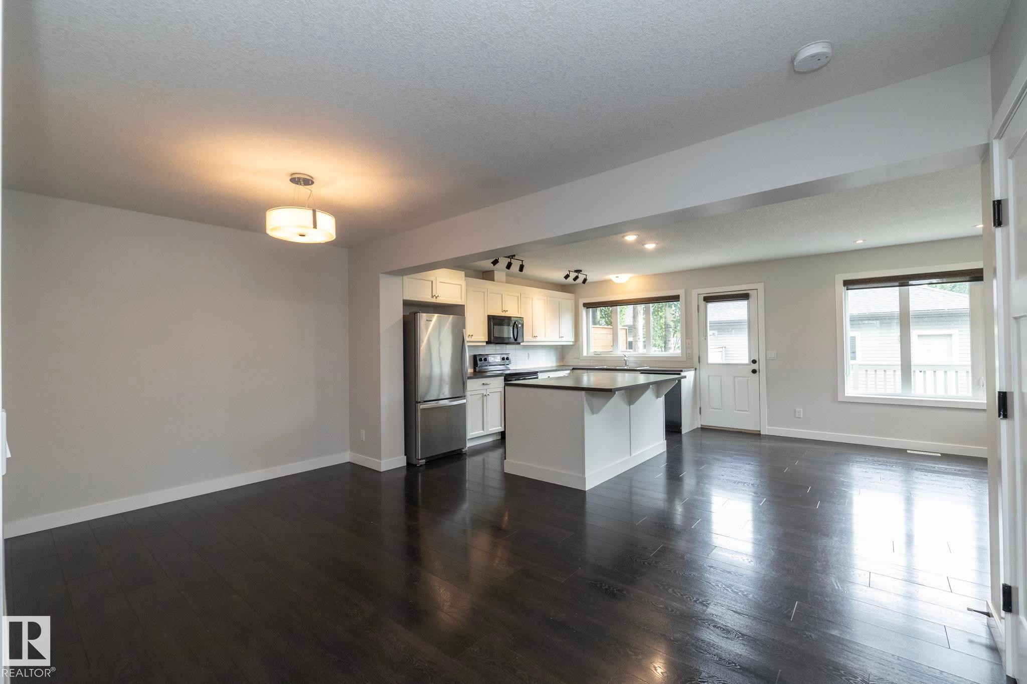Open-concept living space with dark wood-finish flooring, white walls, and a modern ceiling fixture - 55 Michigan Street, Devon, AB