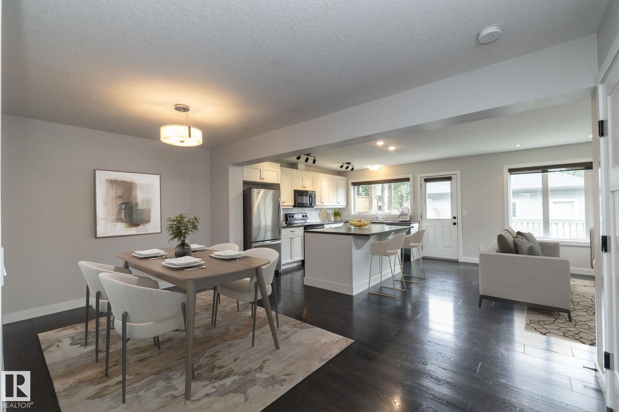 Open-concept living space featuring dark wood-finish flooring, recessed lighting, a kitchen island with seating, stainless steel appliances, and white cabinetry - 55 Michigan Street, Devon, AB