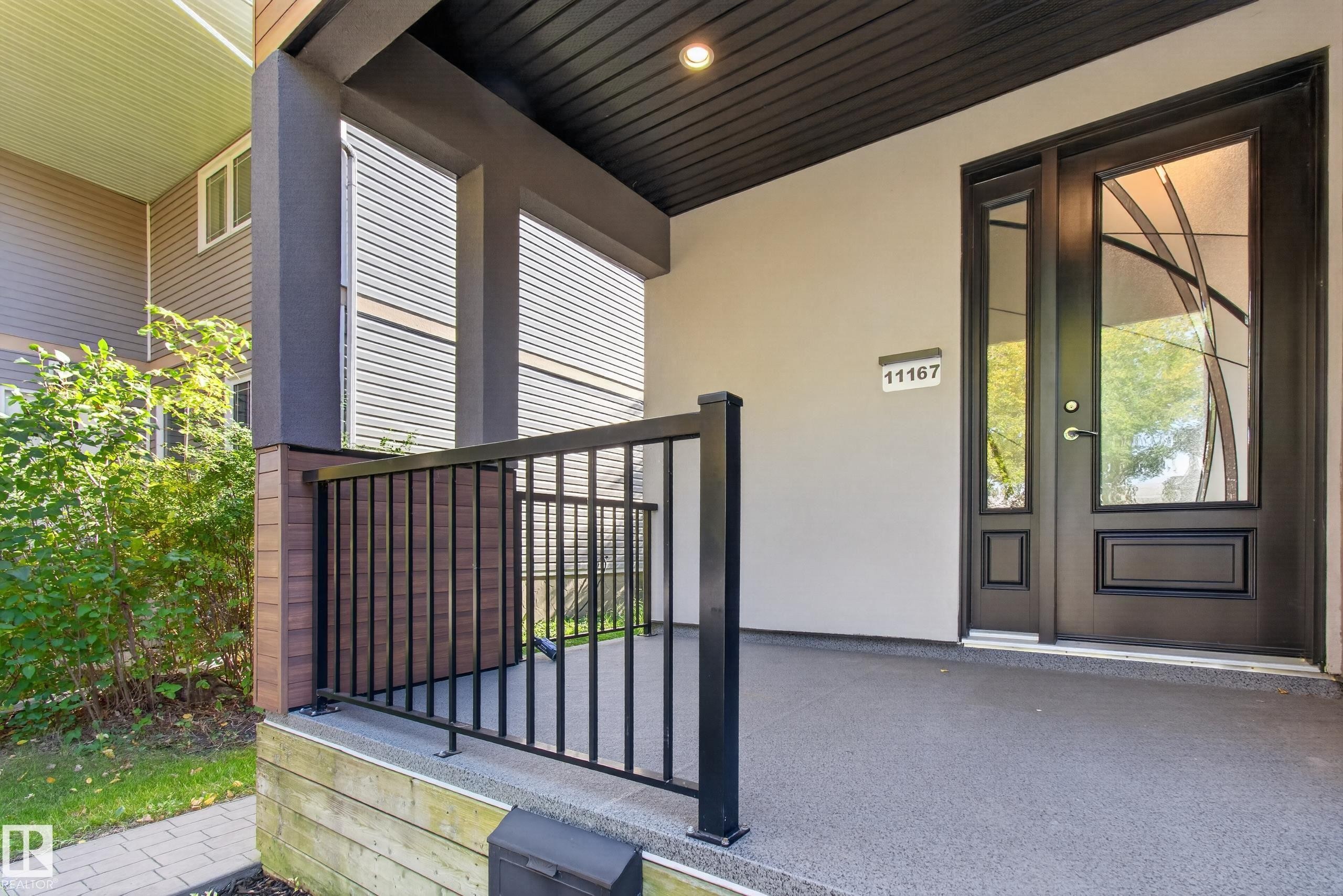 Covered porch with textured gray flooring, black metal railing, and a contemporary entry door with decorative glass - 11167 62 Avenue Nw, Edmonton, AB
