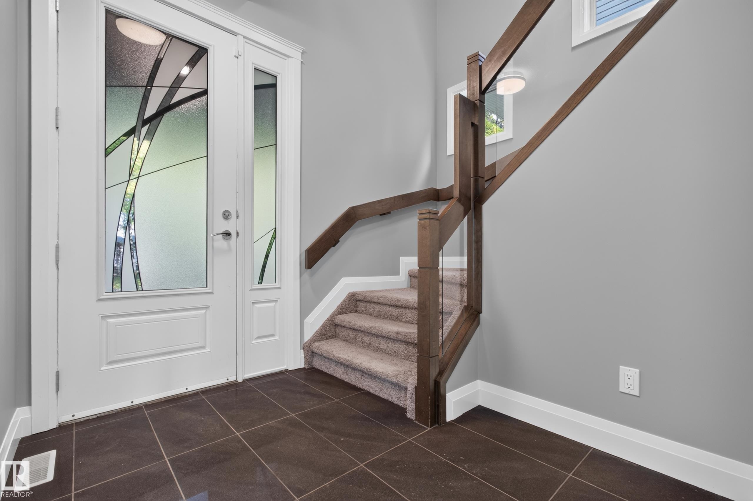 Entryway featuring double doors with decorative glass panels, dark tiled flooring, a carpeted staircase with wood railing, and a window - 11167 62 Avenue Nw, Edmonton, AB