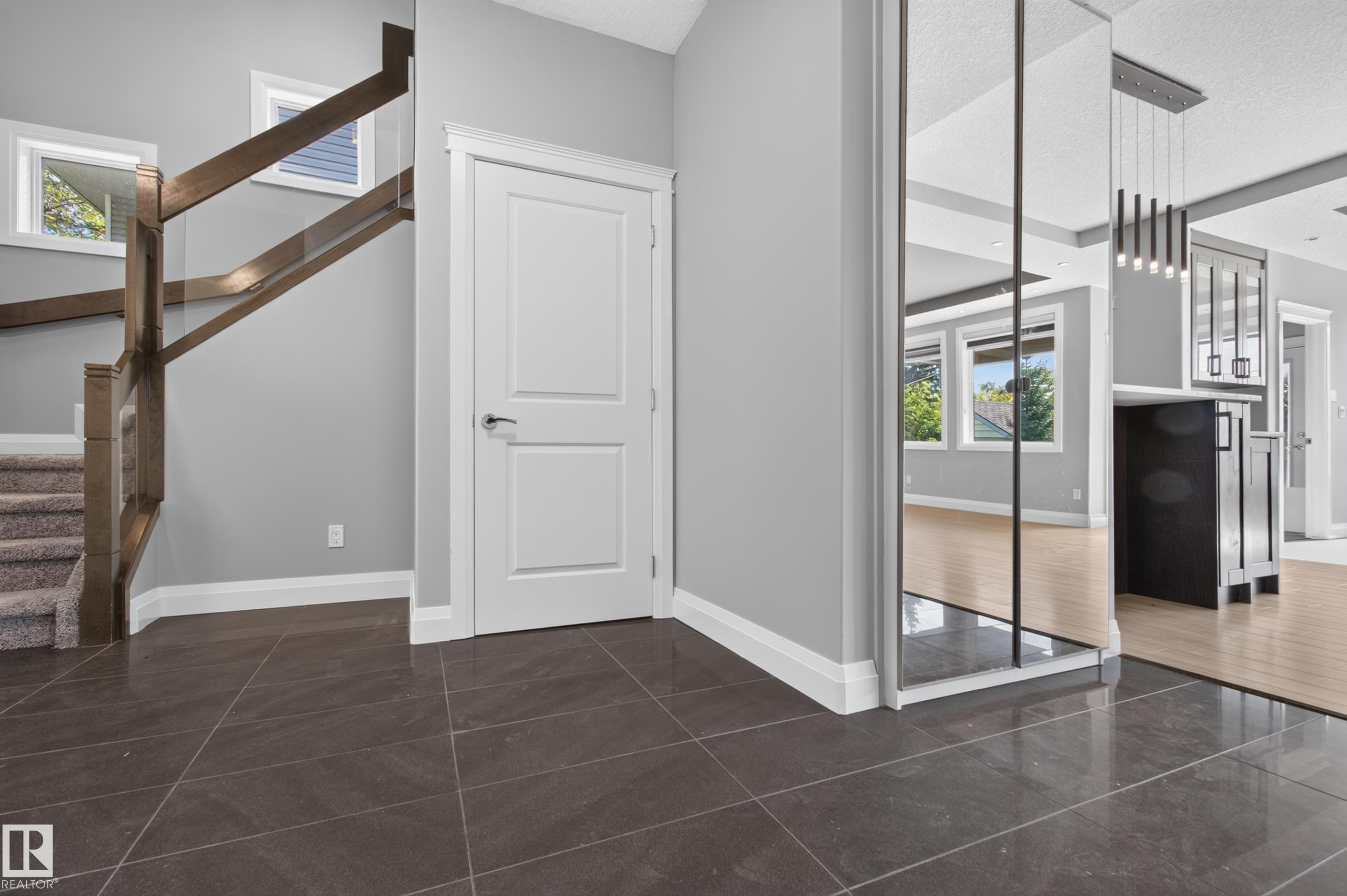 Dark-toned tile flooring, white two-panel door, wood staircase with carpeted treads, and mirrored wall accent - 11167 62 Avenue Nw, Edmonton, AB