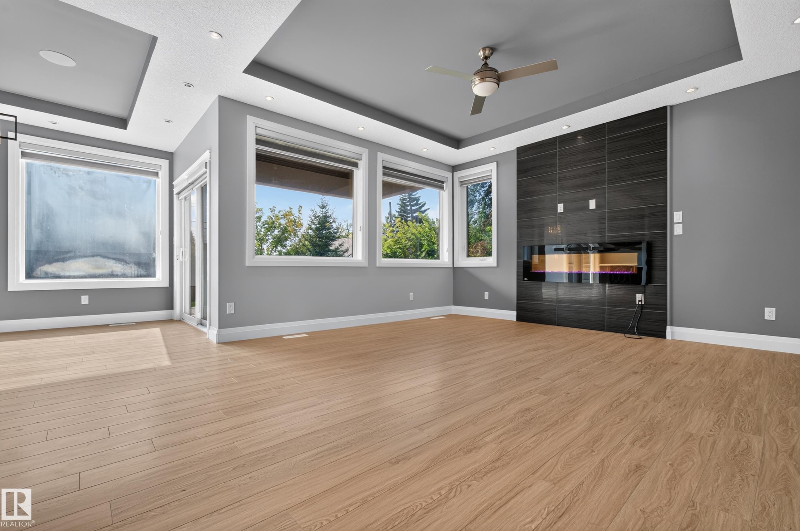 Recessed lighting with layered ceiling details, wood-finish flooring, multiple windows, built-in linear fireplace, and a ceiling fan - 11167 62 Avenue Nw, Edmonton, AB