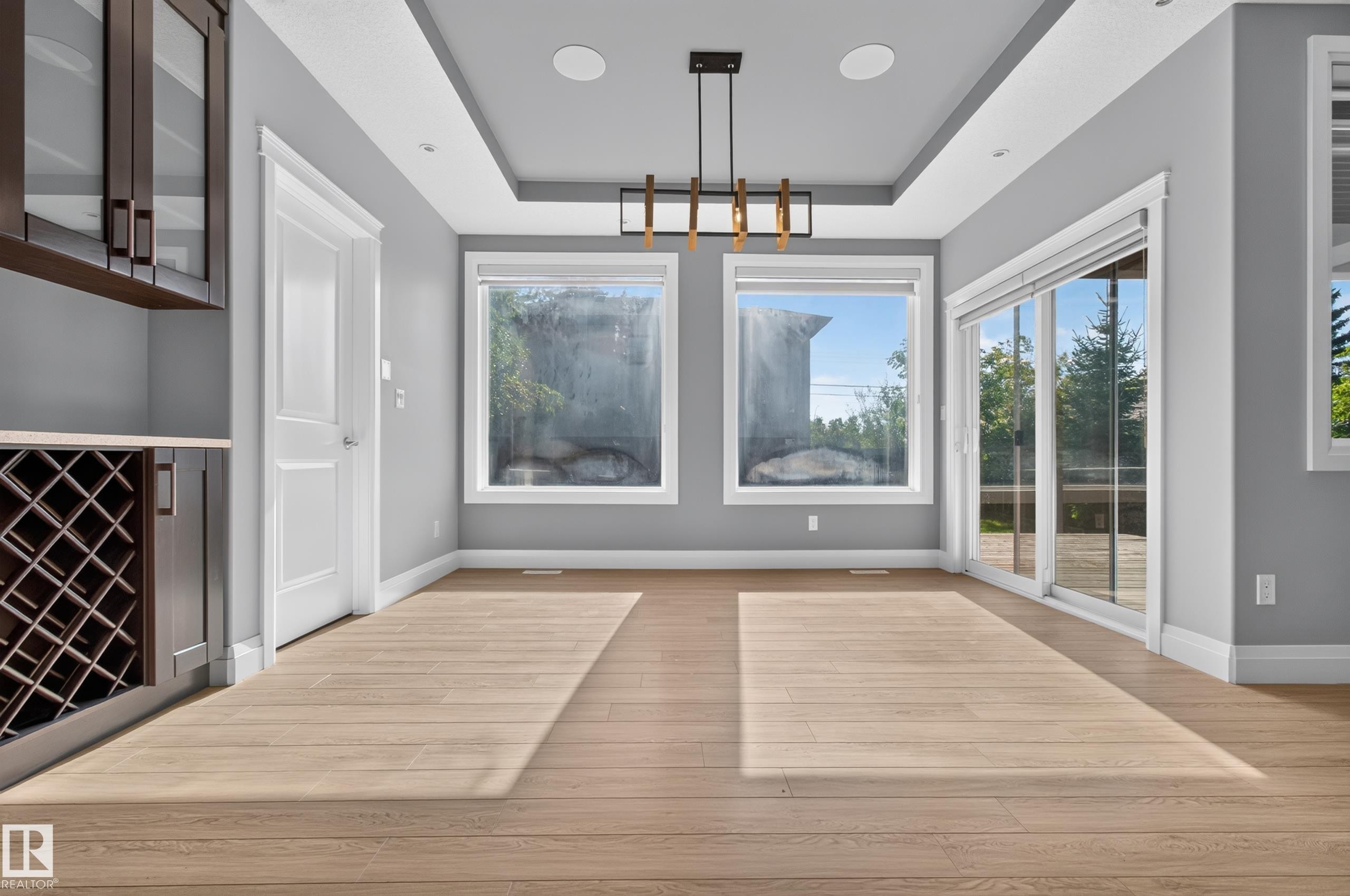 Integrated cabinetry with wine rack, wood-finish flooring, recessed ceiling with contemporary chandelier, multiple windows, and a sliding glass door - 11167 62 Avenue Nw, Edmonton, AB