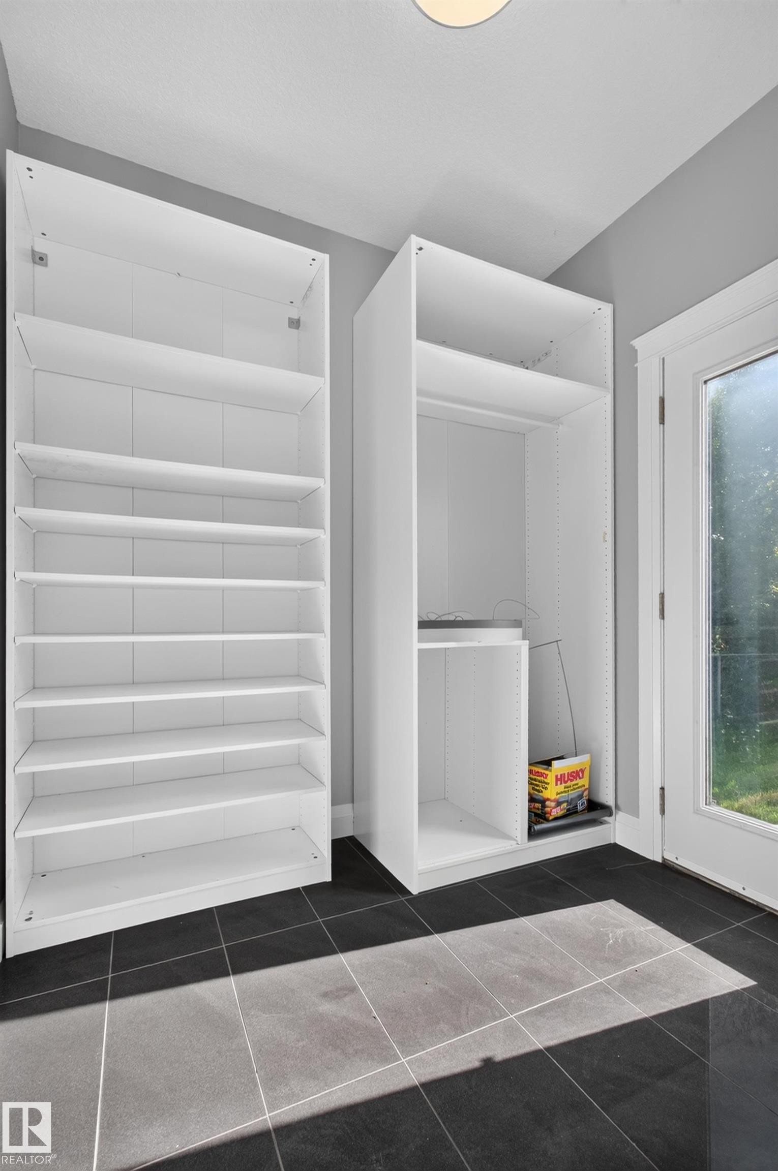 Built-in white storage cabinetry and shelving, dark tile flooring, and a glass-paneled door - 11167 62 Avenue Nw, Edmonton, AB