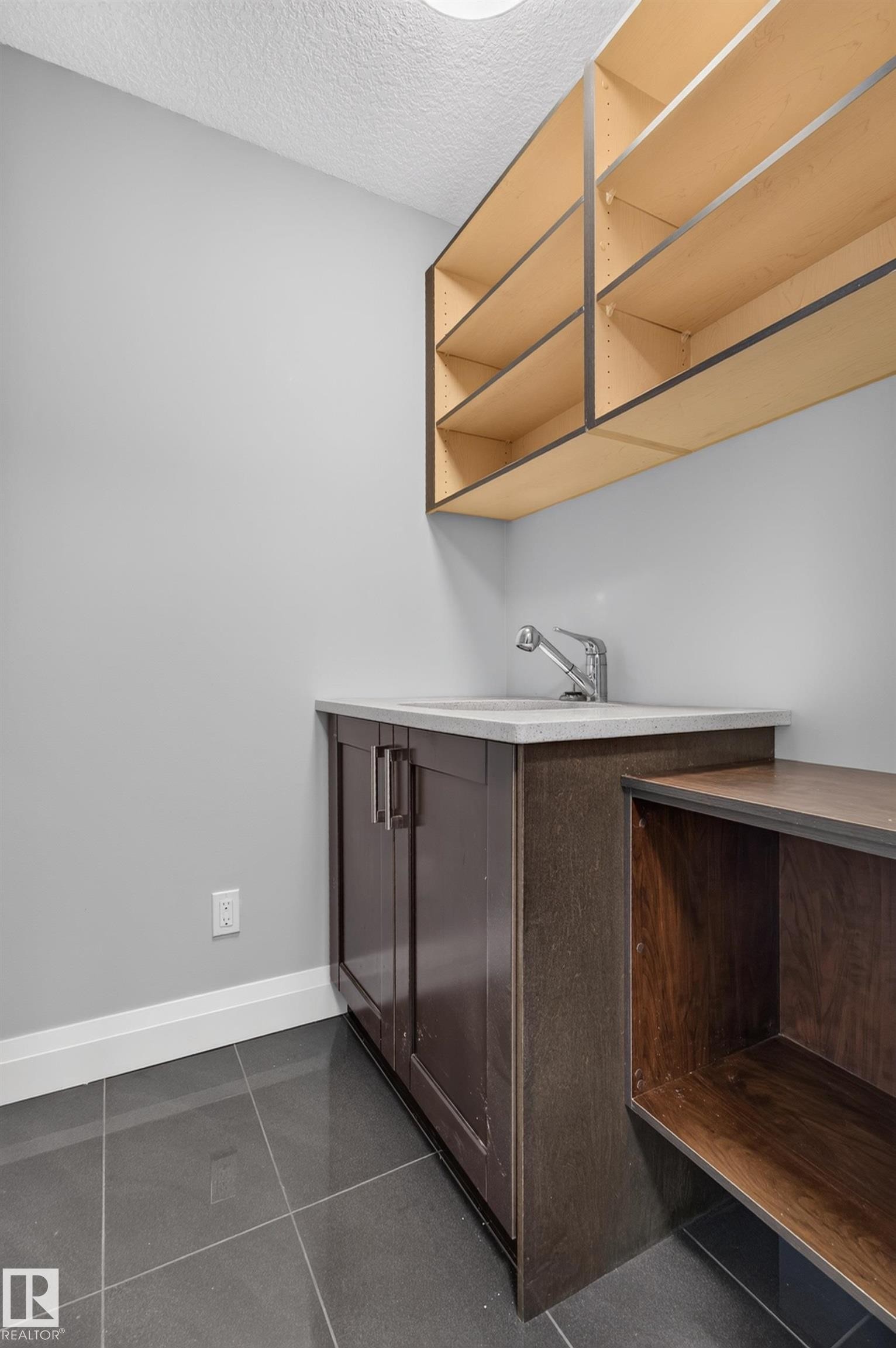 Utility sink with chrome faucet, dark wood-finish cabinetry, light-toned countertop, open shelving, and large format floor tiling - 11167 62 Avenue Nw, Edmonton, AB