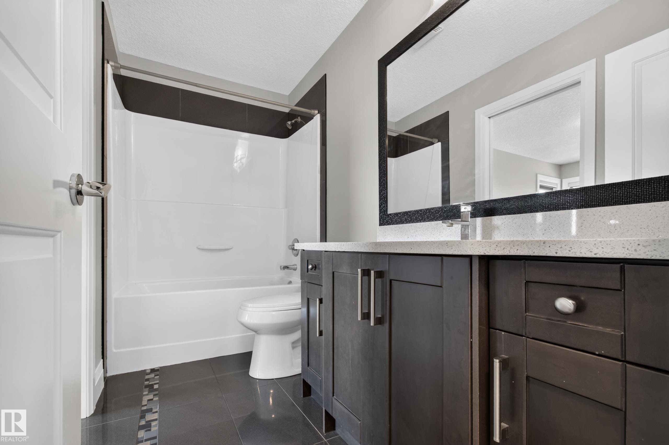 Dark-finish vanity with ample storage and a light-toned countertop, complemented by a decorative framed mirror - 11167 62 Avenue Nw, Edmonton, AB