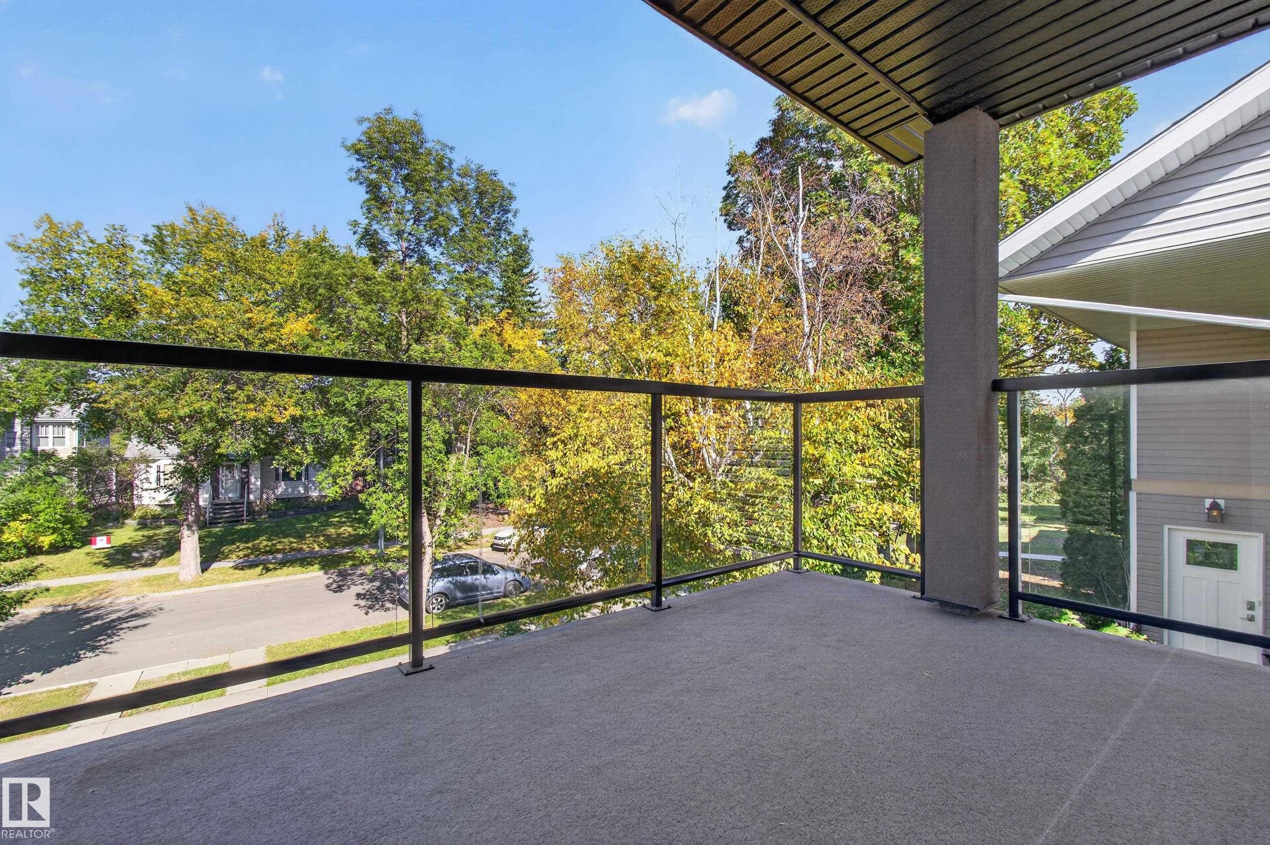 Balcony with glass panel railing and textured flooring, complemented by a slatted ceiling overhang - 11167 62 Avenue Nw, Edmonton, AB