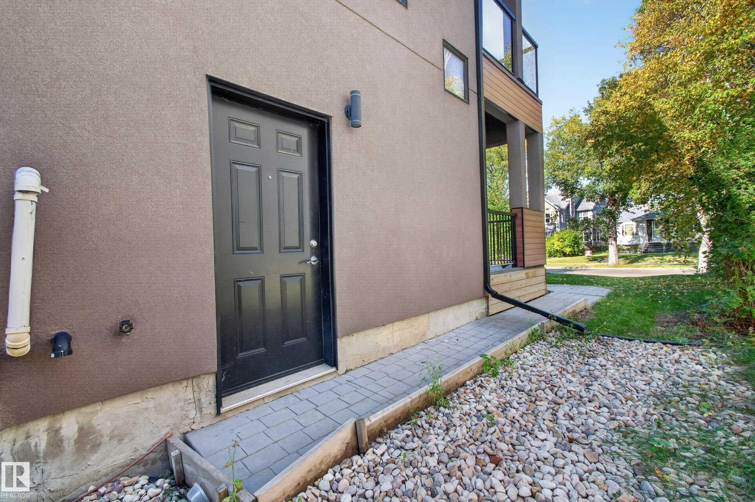 Stucco exterior with a black panel door, paver walkway, and gravel landscaping - 11167 62 Avenue Nw, Edmonton, AB