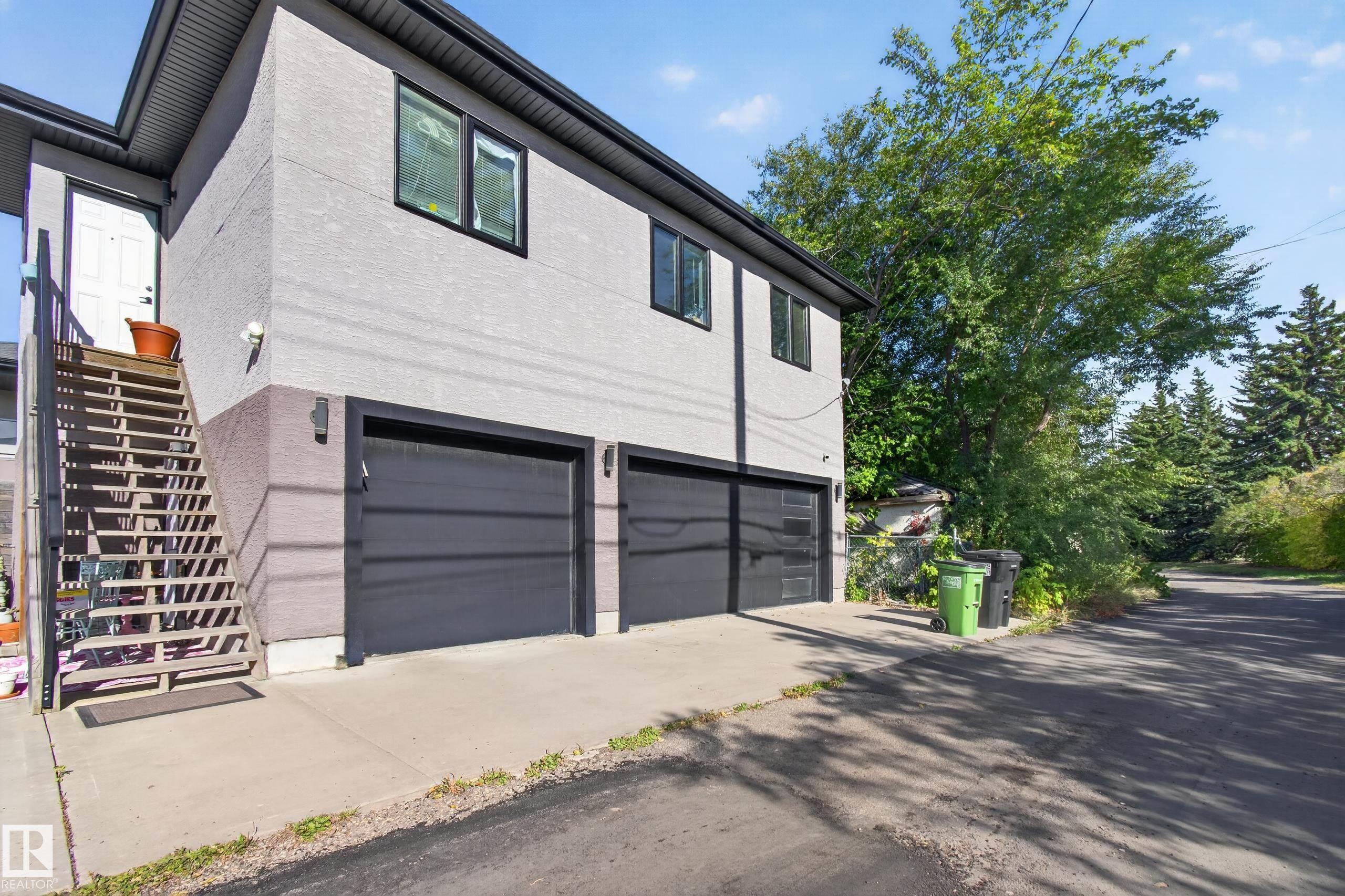 Stucco exterior with black trim windows, dual garage bays, and exterior staircase entry - 11167 62 Avenue Nw, Edmonton, AB
