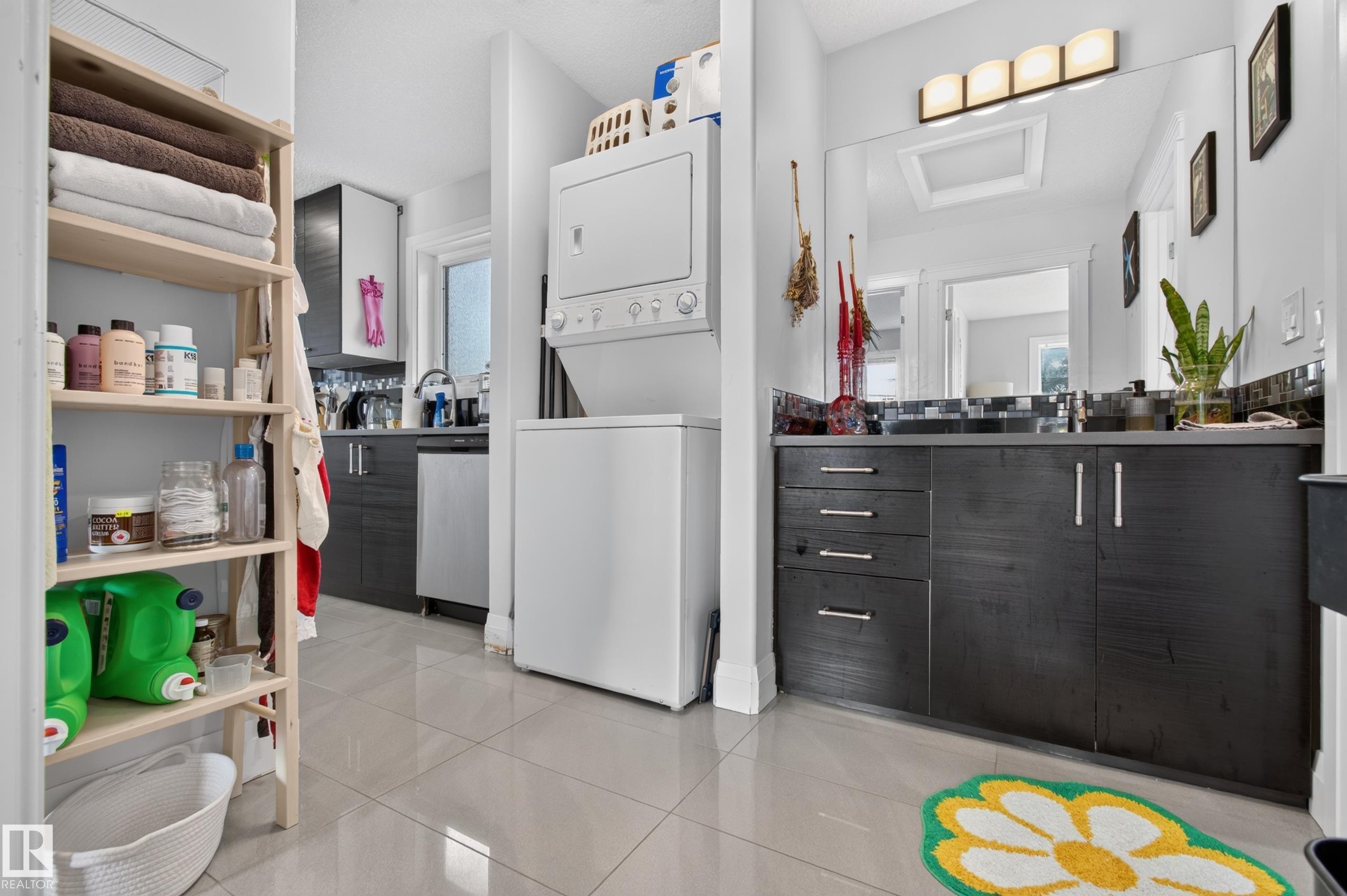Tile flooring throughout, stacked washer and dryer, dark wood-finish vanity with drawer storage, large wall-mounted mirror, and a wall-mounted light fixture - 11167 62 Avenue Nw, Edmonton, AB