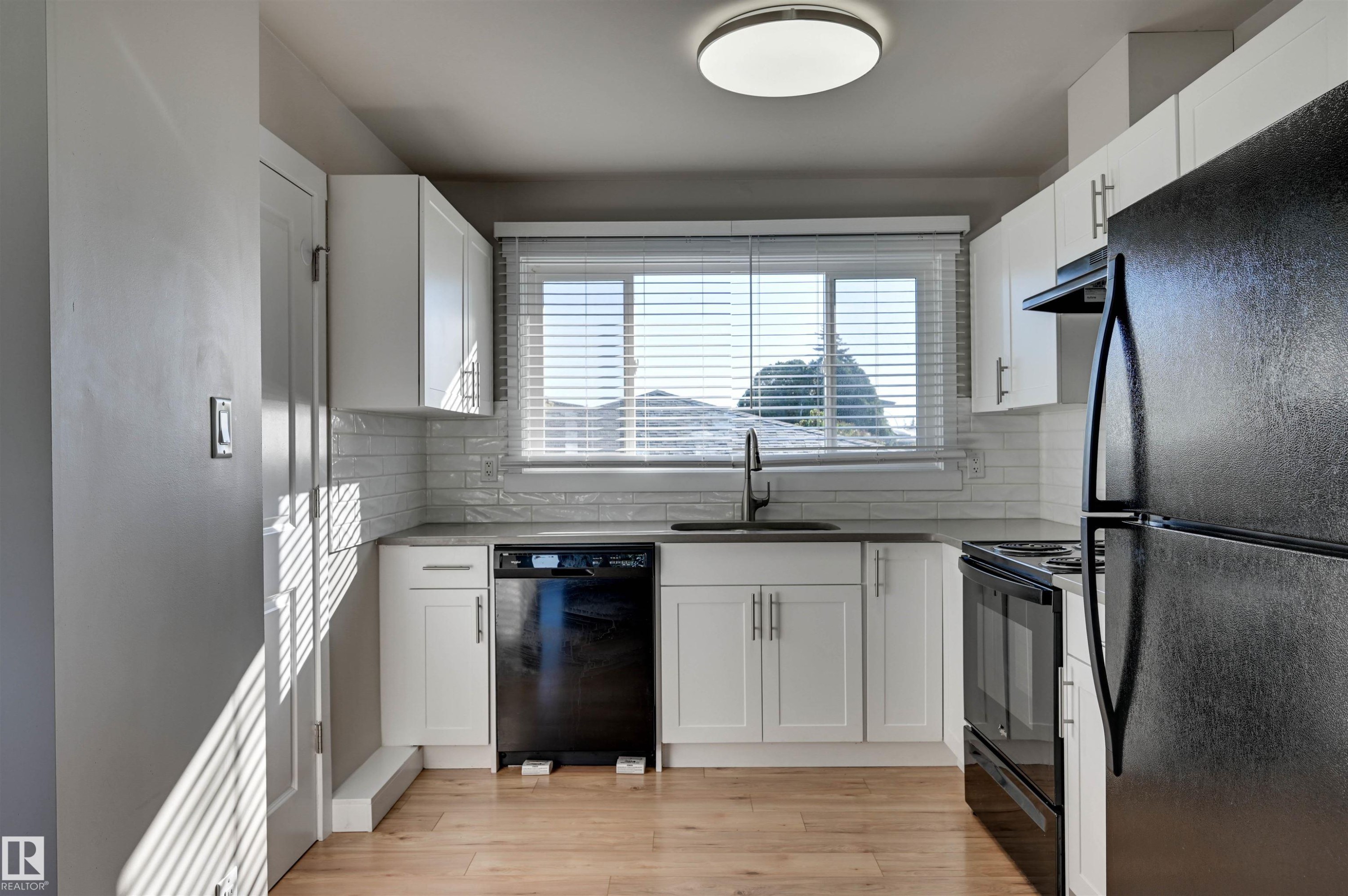 Well-appointed kitchen featuring white cabinetry, subway tile backsplash, dark countertops, and wood-finish flooring - 13815 88 Street Nw, Edmonton, AB