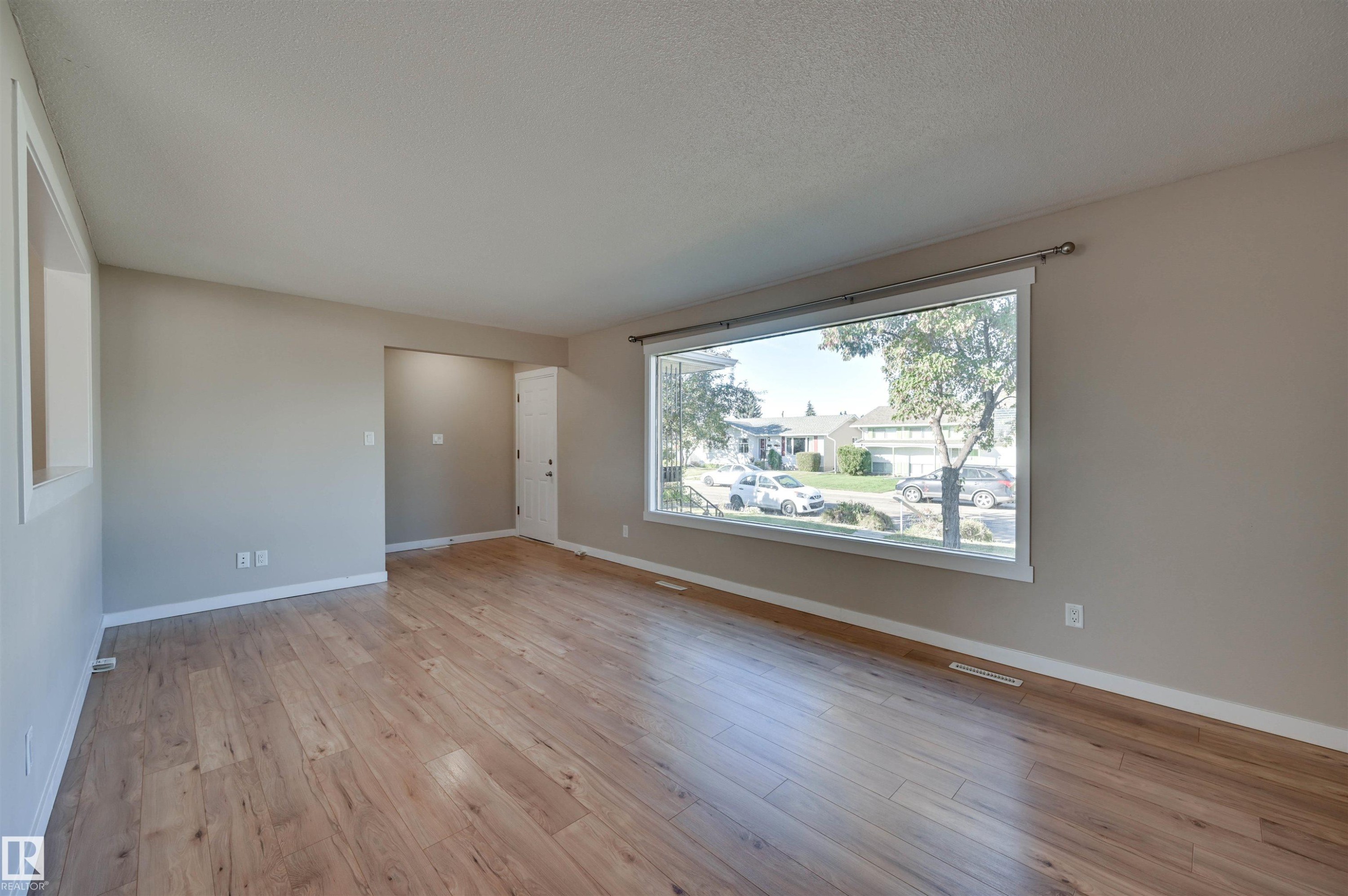 Wood-finish flooring throughout, complemented by a large picture window and neutral wall finishes - 13815 88 Street Nw, Edmonton, AB