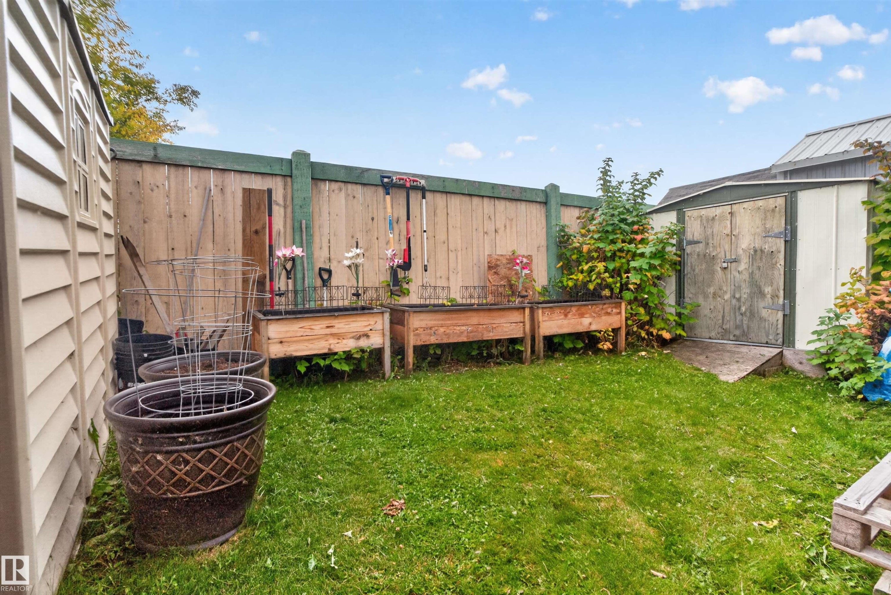 Fenced backyard featuring a storage shed, a second utility shed with horizontal siding, and two raised garden beds - 1405 53222 Range Road 272, Rural Parkland County, AB