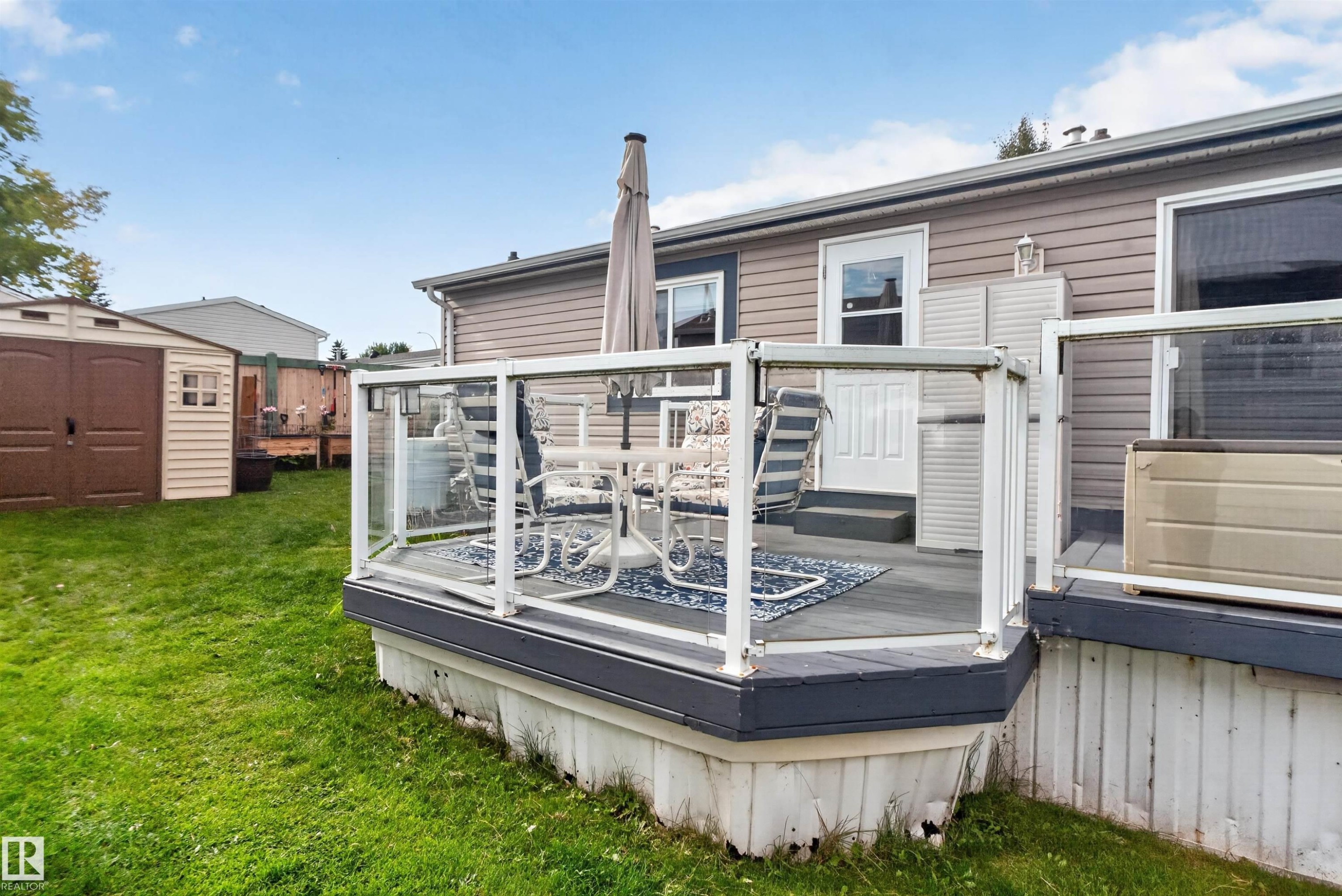 Outdoor deck with glass panel railing and composite decking, featuring a white exterior door, and vinyl siding - 1405 53222 Range Road 272, Rural Parkland County, AB