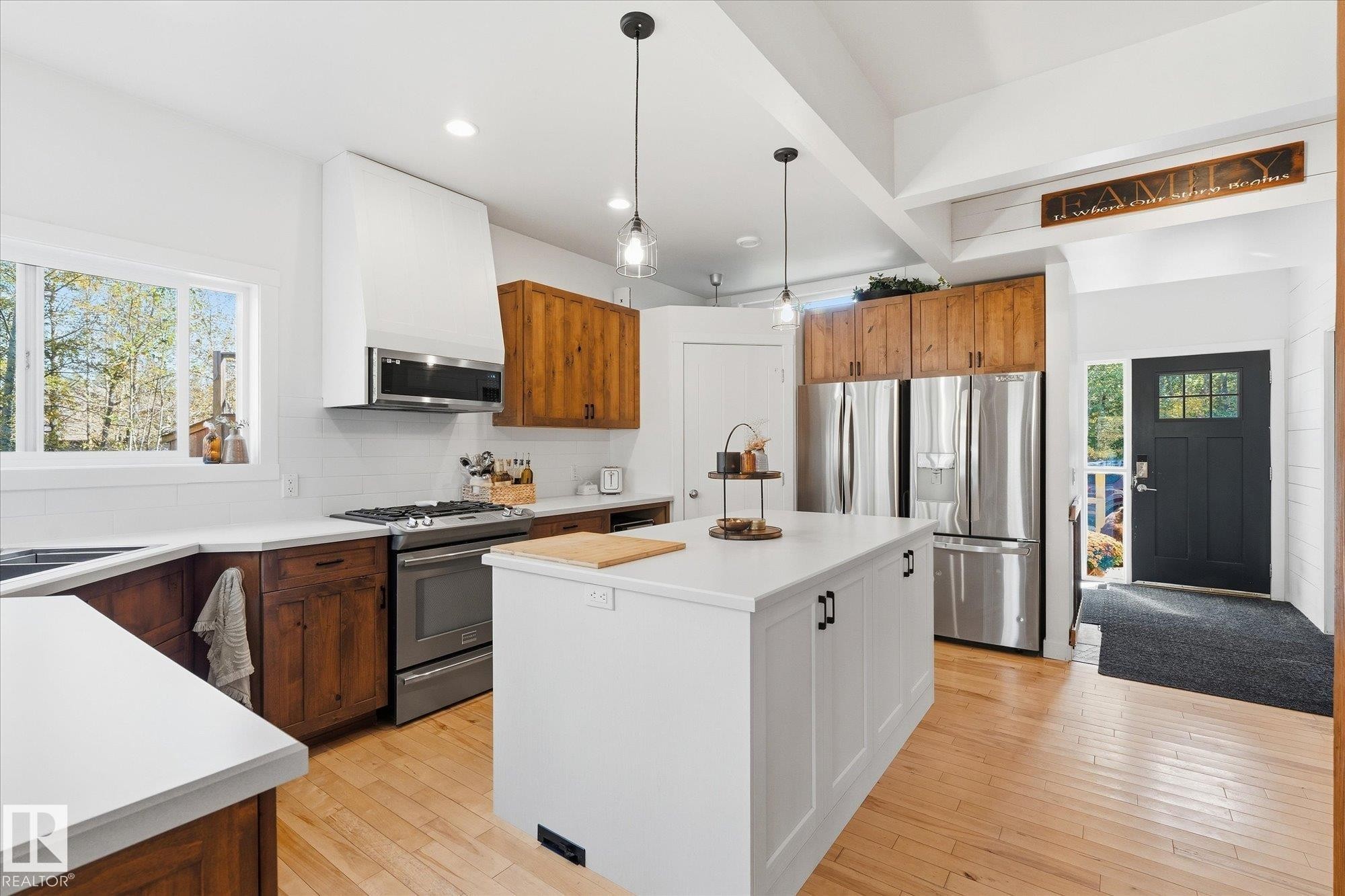 Kitchen featuring hardwood flooring, a center island with a white countertop, stainless steel appliances, and a gas range - #45 53122 Rge Road 14, Rural Parkland County, AB