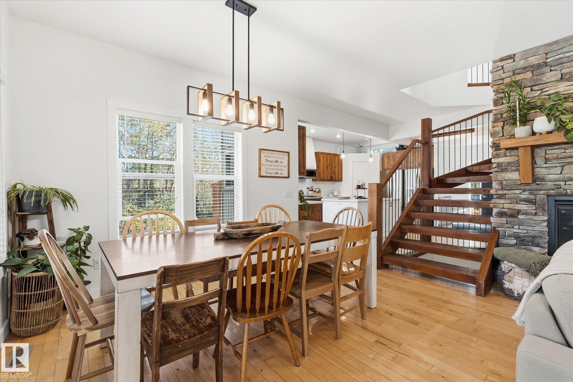 Hardwood flooring throughout, stone-clad fireplace, open-tread wood staircase with metal balusters, contemporary linear chandelier, and multiple windows with natural light - #45 53122 Rge Road 14, Rural Parkland County, AB