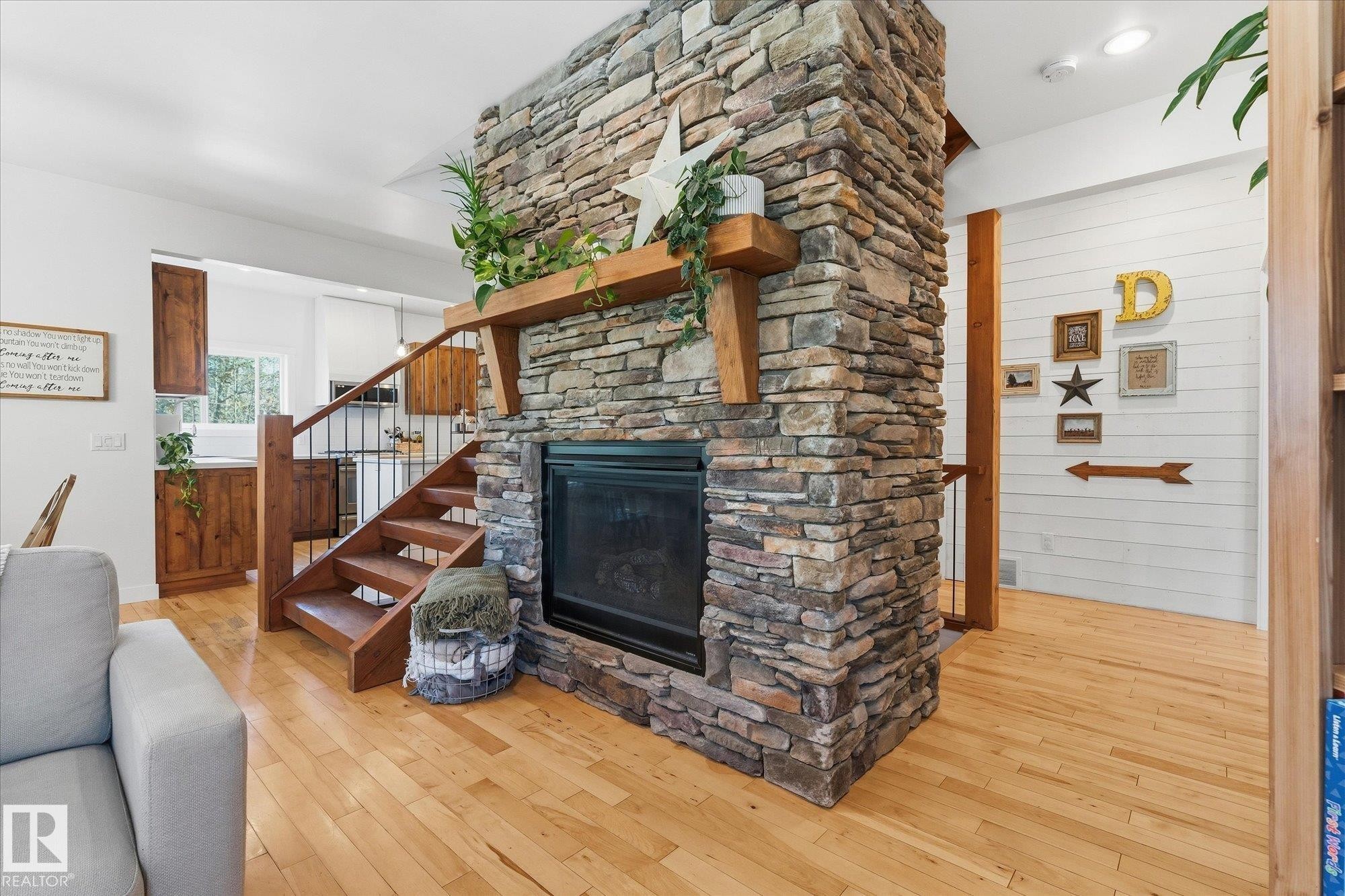 Stone-clad fireplace with wood mantel, hardwood flooring, and wood stairway with metal balusters - #45 53122 Rge Road 14, Rural Parkland County, AB