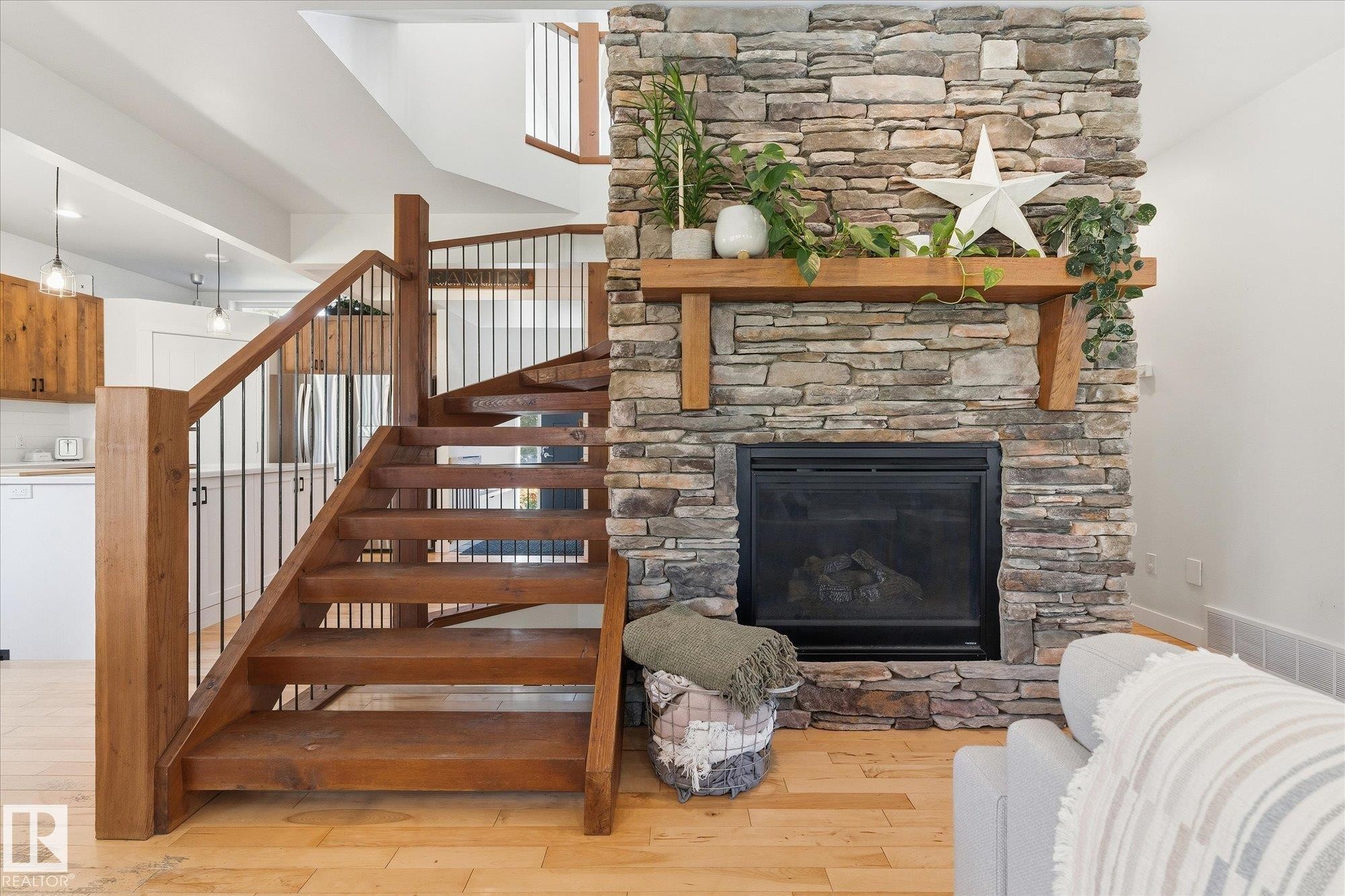 Wood staircase with black metal balusters, stacked stone fireplace, wood mantel, and light wood-finish flooring - #45 53122 Rge Road 14, Rural Parkland County, AB