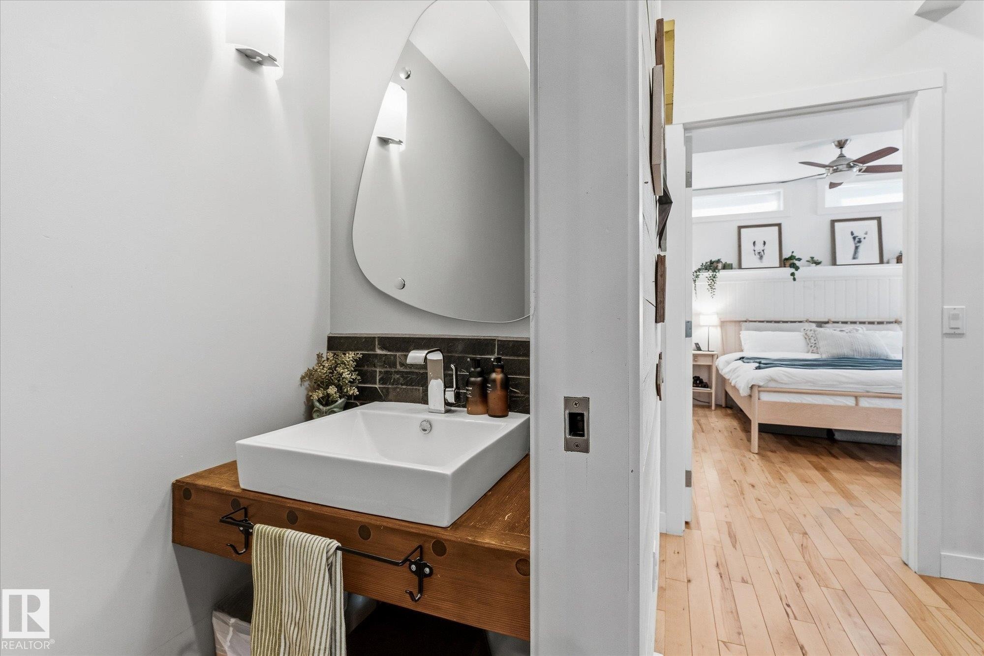 Floating wood-finish vanity with a rectangular vessel sink and wall-mounted faucet, complemented by a unique mirror - #45 53122 Rge Road 14, Rural Parkland County, AB