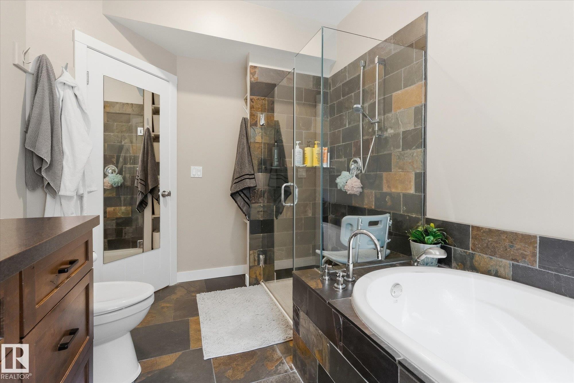 Walk-in shower with glass enclosure, freestanding soaking tub, and natural stone-look tile flooring - #45 53122 Rge Road 14, Rural Parkland County, AB