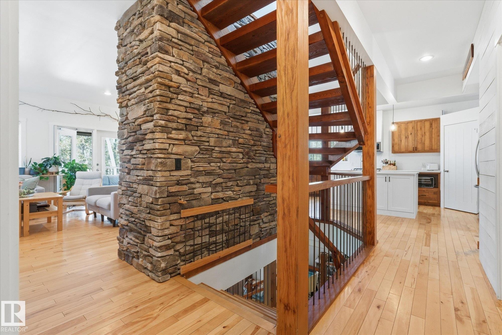 Stone accent wall, wood-finish flooring, open-tread staircase with wood newel posts, black metal balusters, and white cabinetry with wood-finish upper cabinets - #45 53122 Rge Road 14, Rural Parkland County, AB