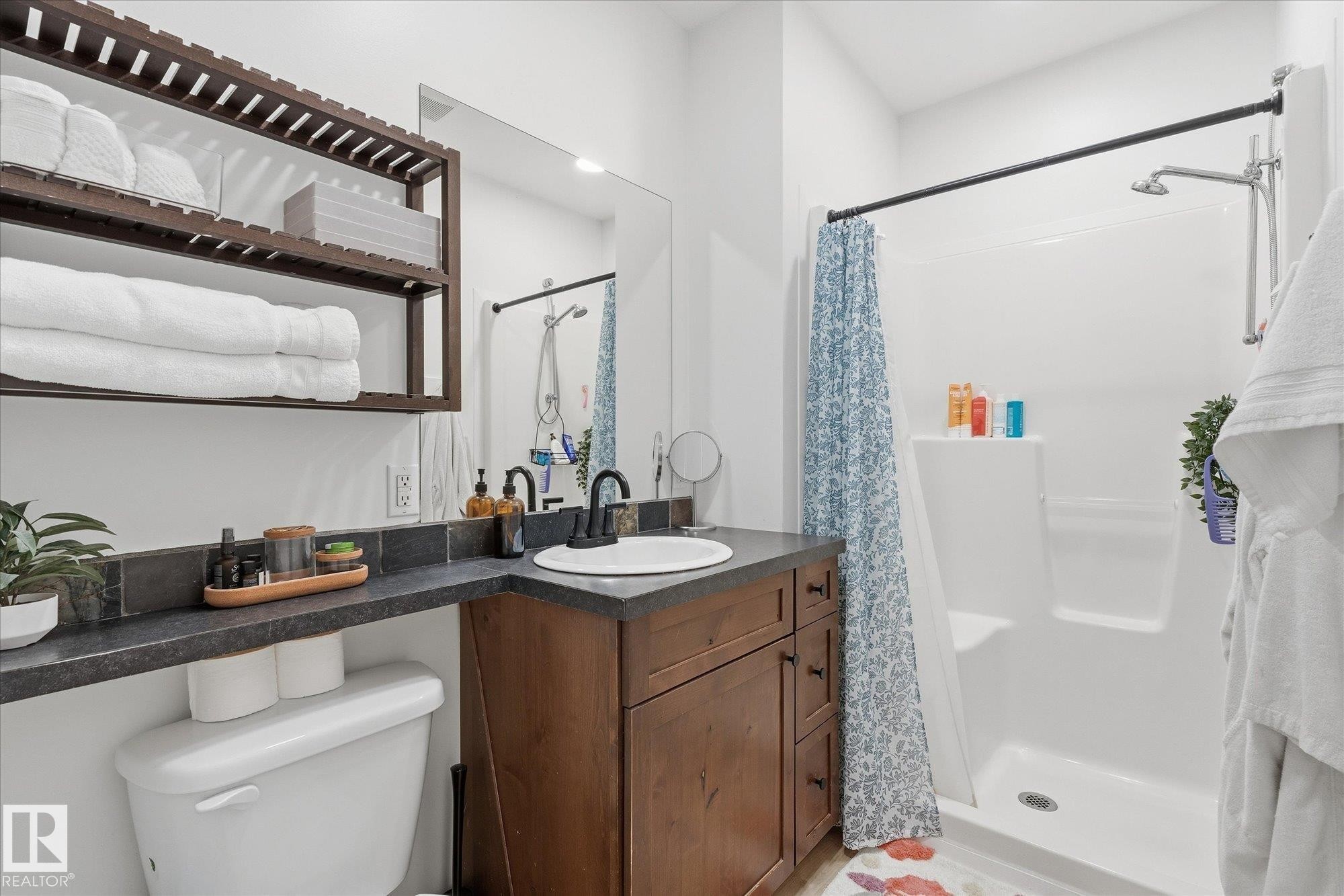 Built-in open shelving, dark wood-finish vanity with drawer storage, integrated sink, dark countertop, and stand-up shower with a dark finish shower rod - #45 53122 Rge Road 14, Rural Parkland County, AB