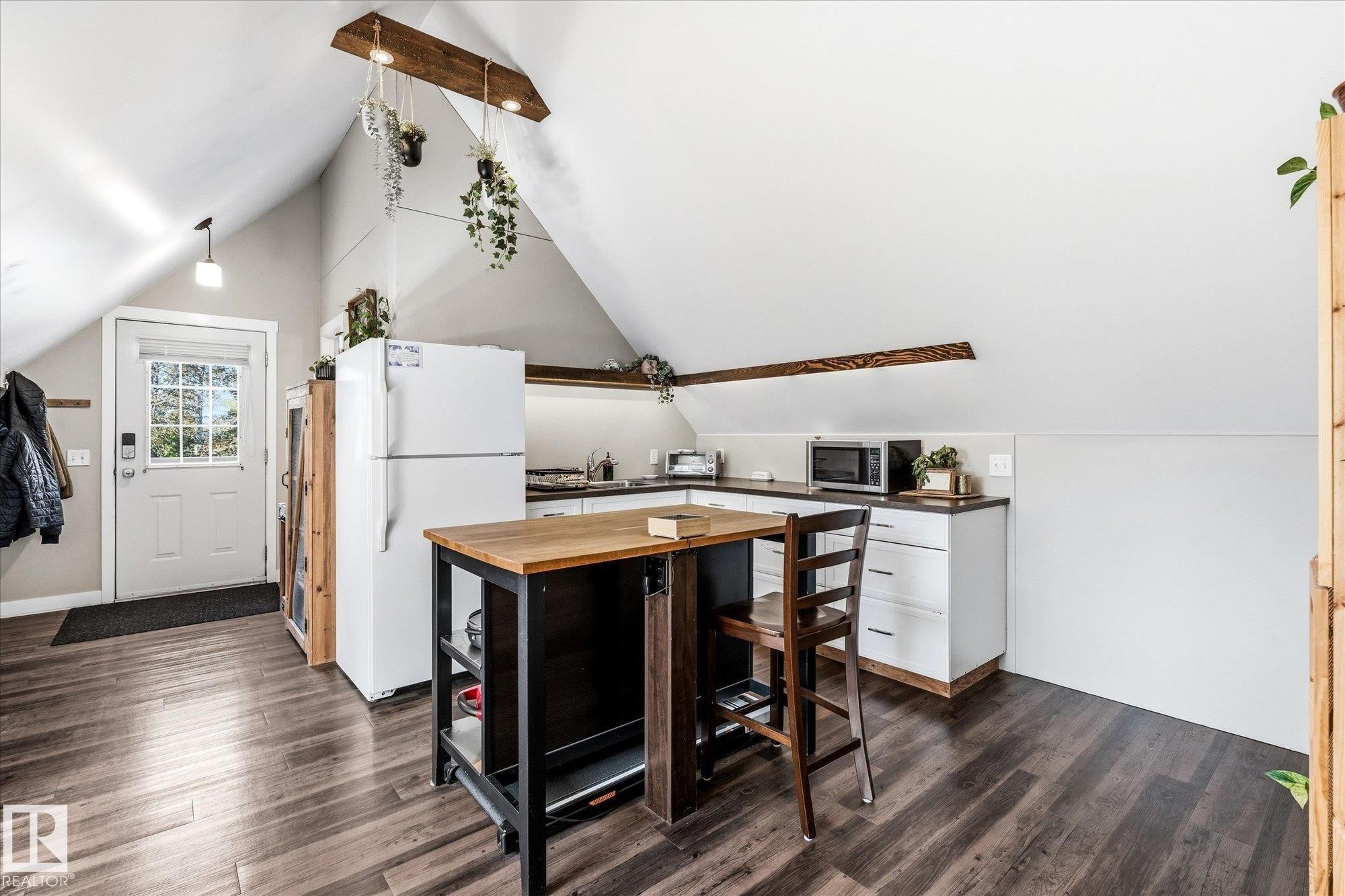 Angled ceilings with exposed wood beams, wood-finish flooring, white cabinetry, dark countertops, and a white paneled door with glass inserts - #45 53122 Rge Road 14, Rural Parkland County, AB