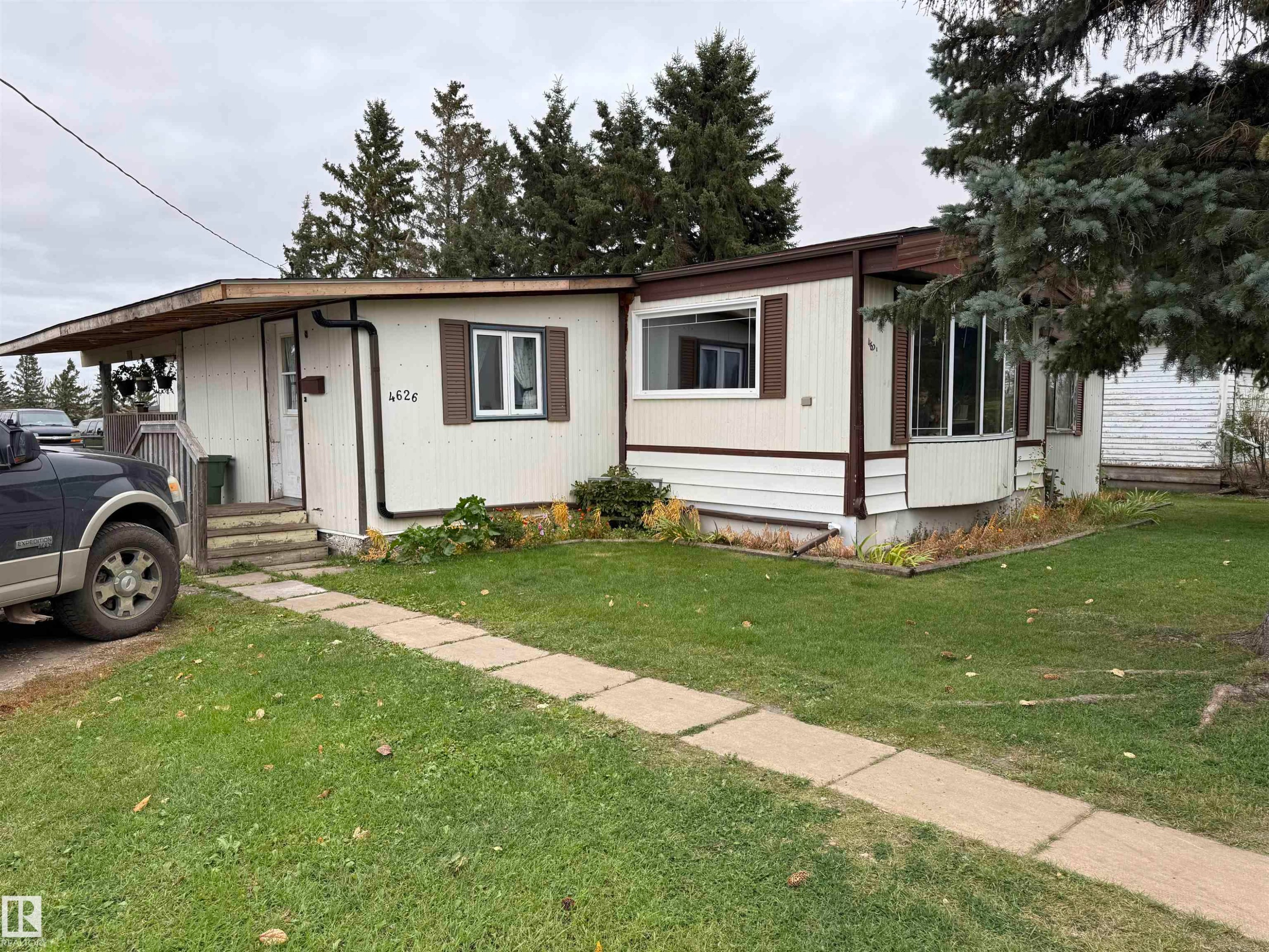 Exterior featuring light-colored siding with brown trim, covered front entry, bay window, and a concrete paver walkway - 4626 51 Avenue, Willingdon, AB