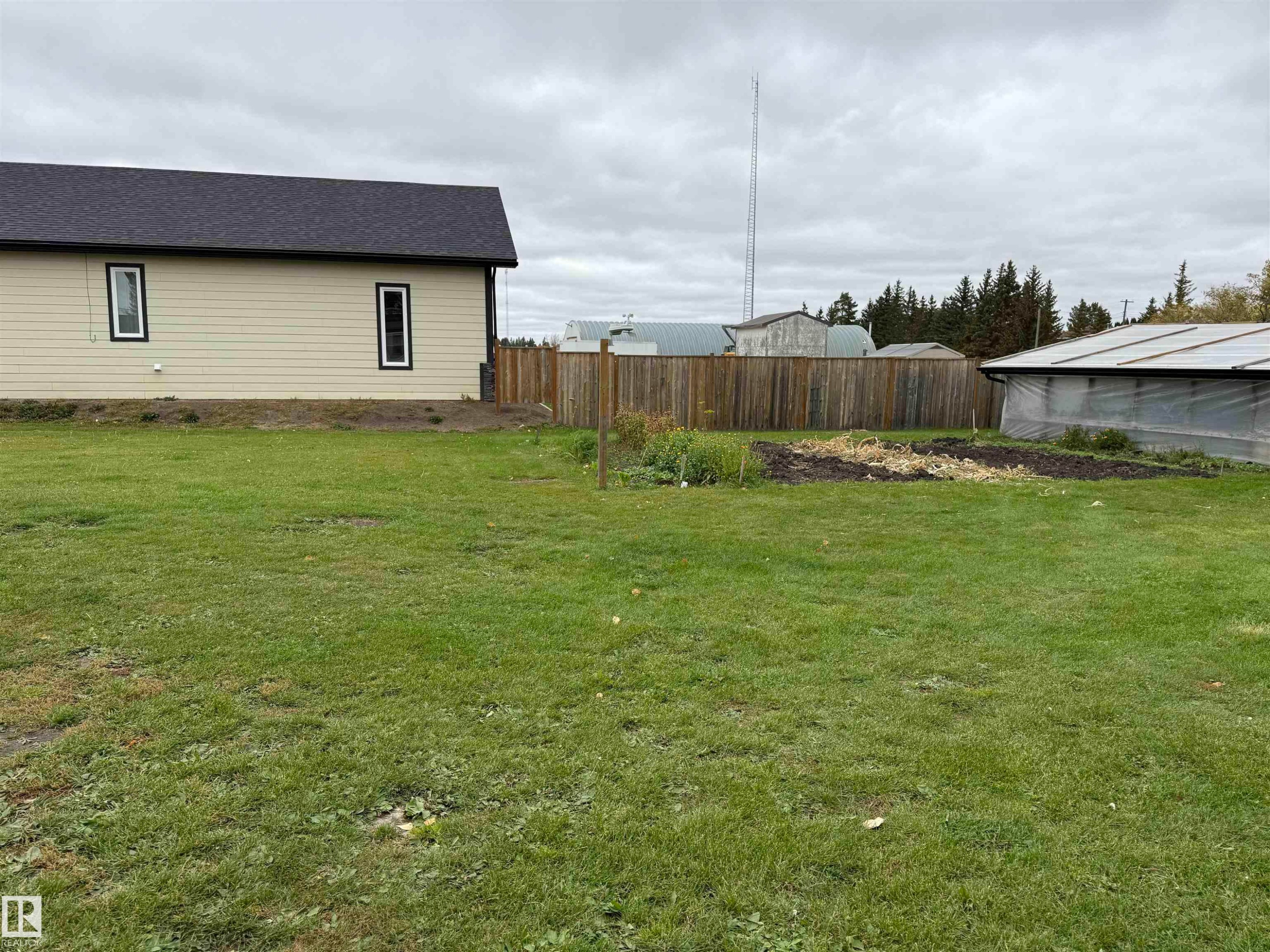 Expansive green lawn with a wood fence, featuring a garden bed and a greenhouse structure - 4626 51 Avenue, Willingdon, AB