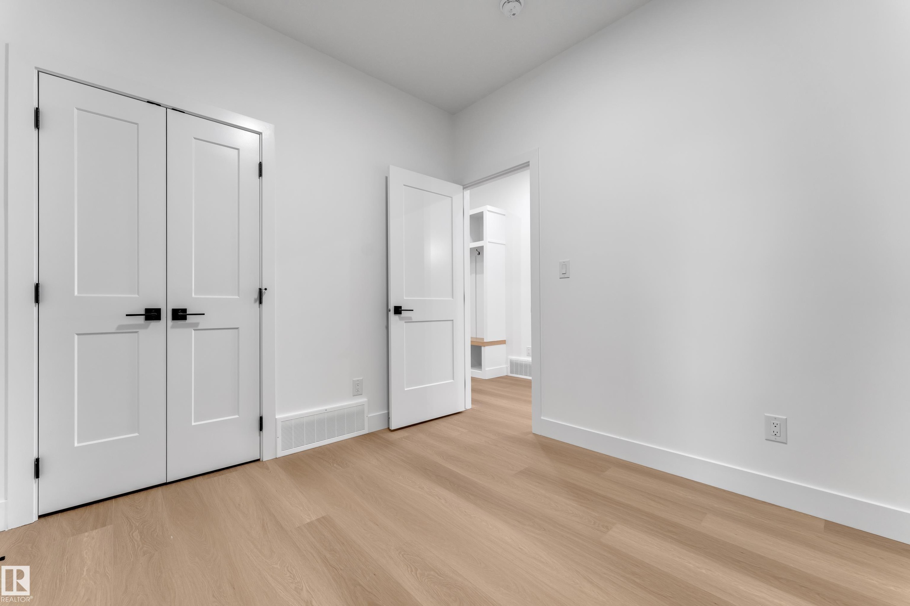 Light wood-finish flooring, white walls, white trim, and white paneled doors with matte black hardware - 794 Bank Drive, Leduc, AB
