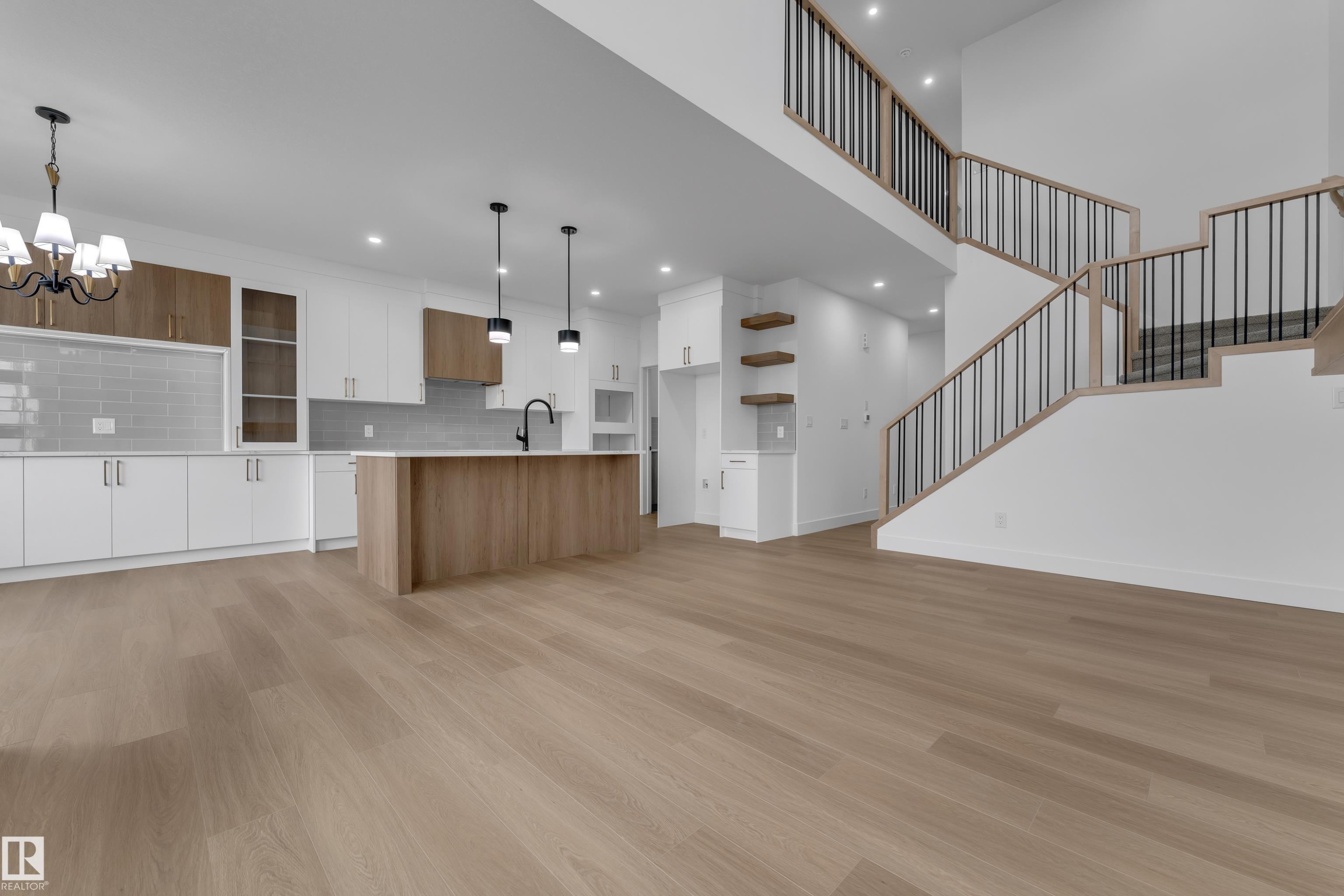 Open-concept living area featuring wood-finish flooring, a contemporary kitchen with white and wood-tone cabinetry, a central island, and a staircase with open risers and metal balusters - 794 Bank Drive, Leduc, AB